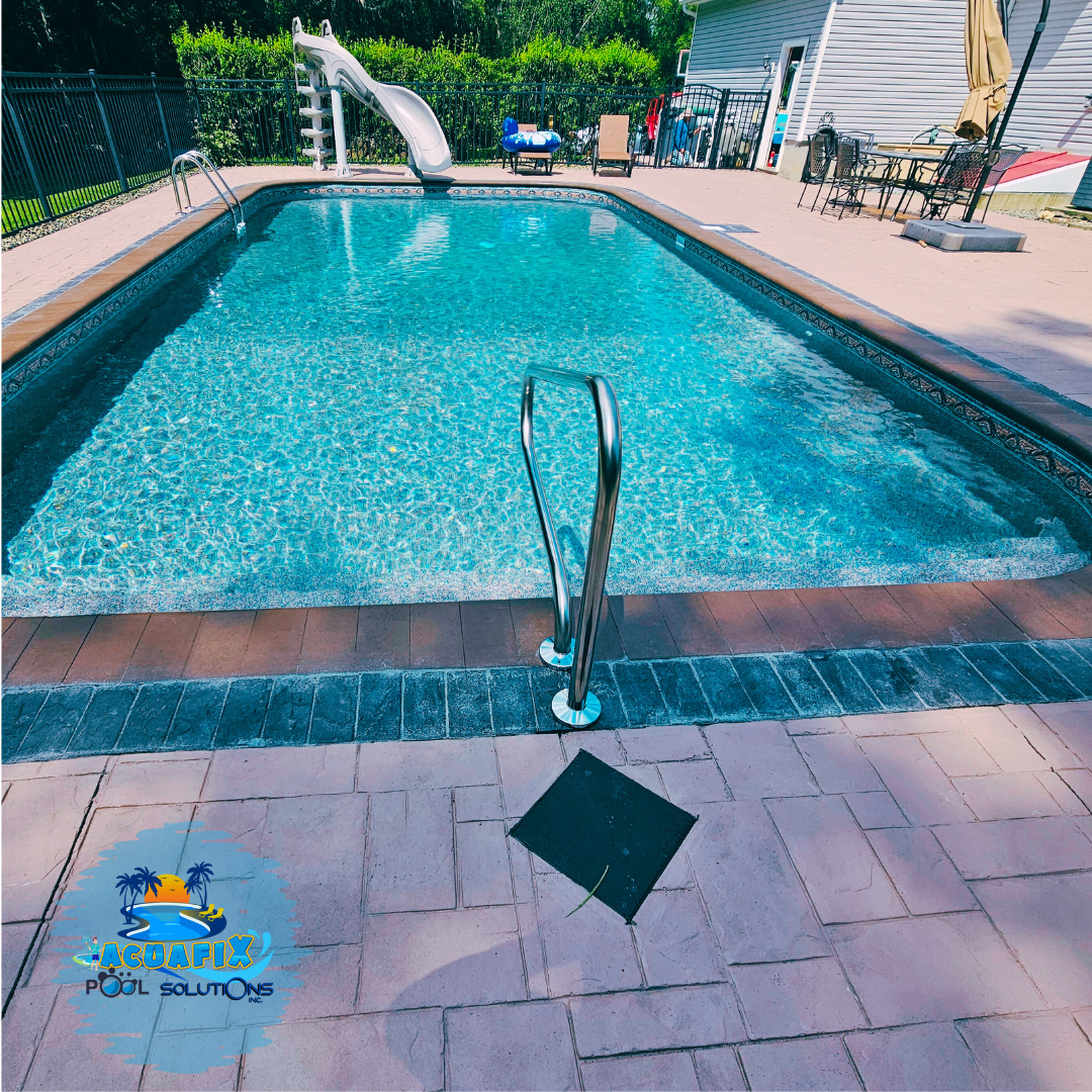 Outdoor swimming pool with clear blue water, metal handrail, tiled deck, and slide in the background Outdoor swimming pool with clear blue water, metal handrail, tiled deck, and slide in the background