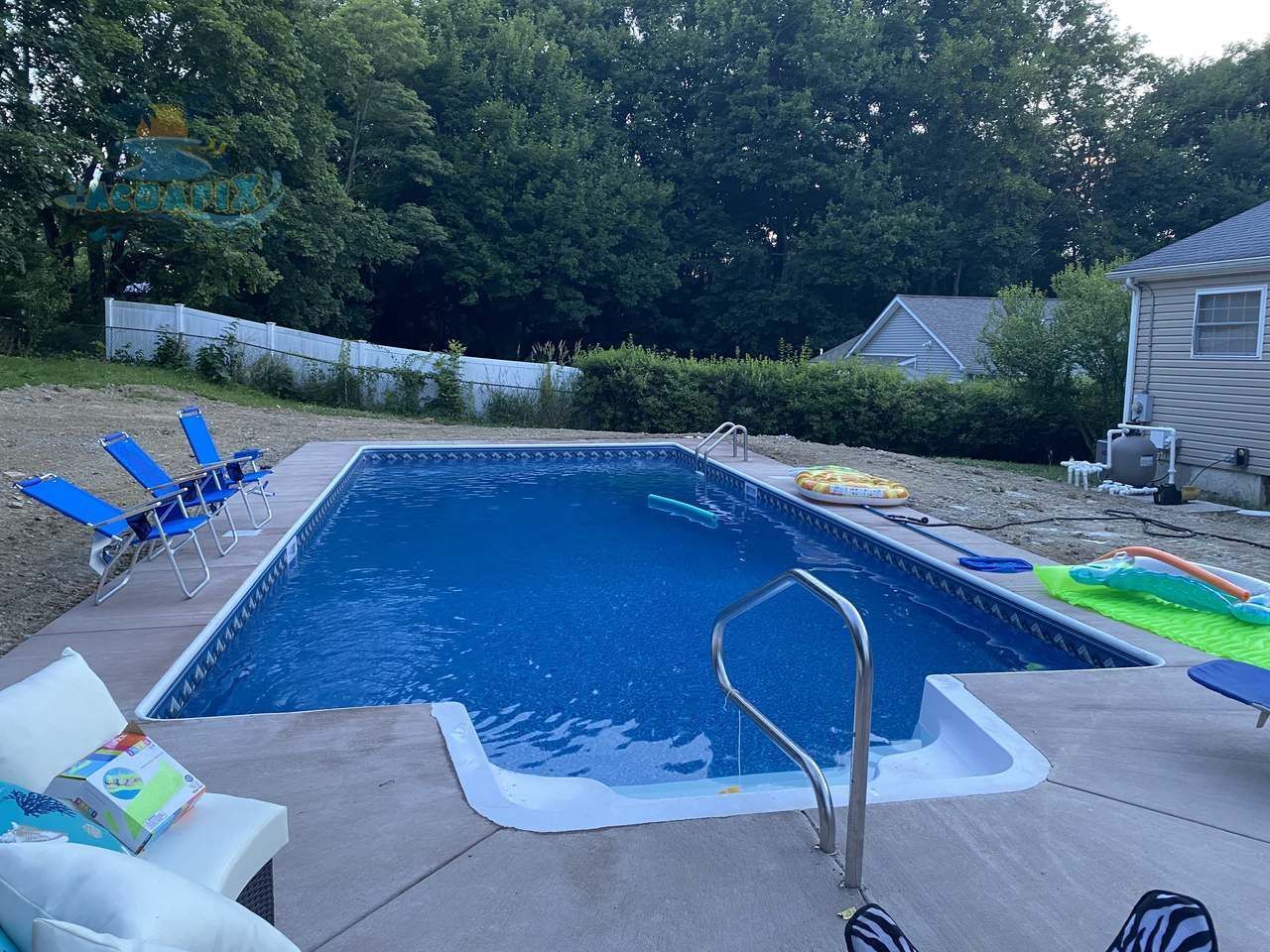 Backyard swimming pool with blue chairs, pool steps, and a diving board at dusk