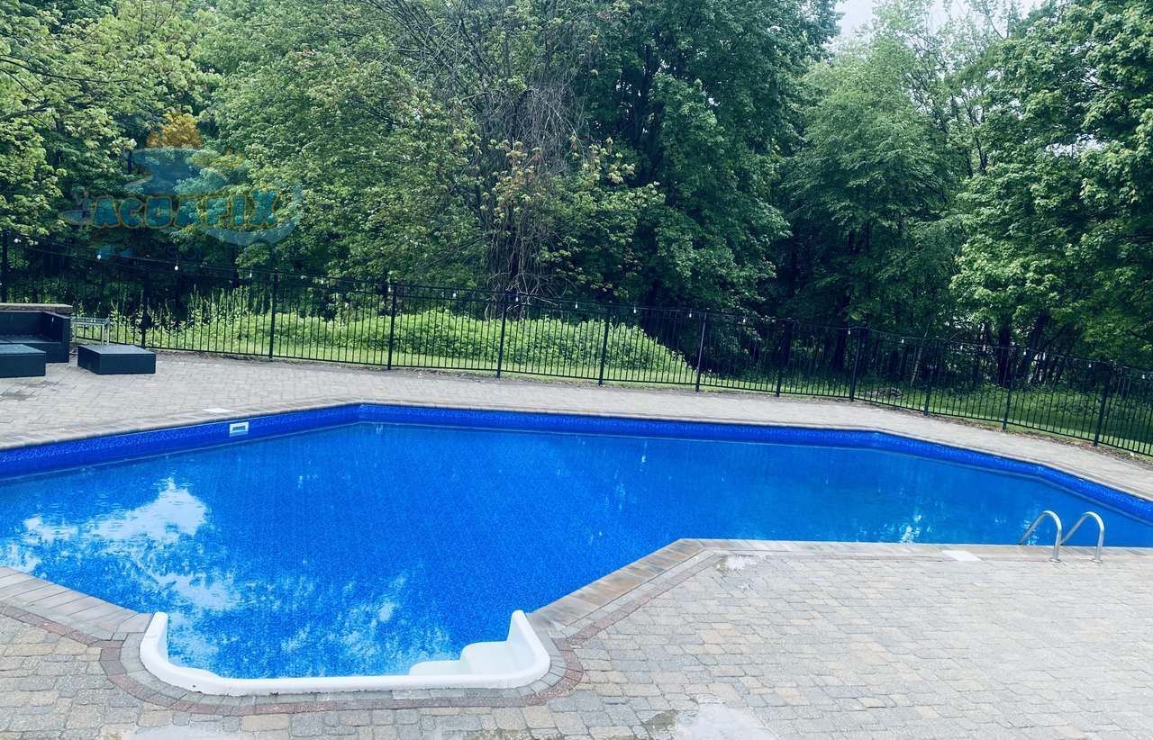Blue backyard swimming pool beside a stone patio, with green trees in the background. Blue backyard swimming pool beside a stone patio, with green trees in the background.