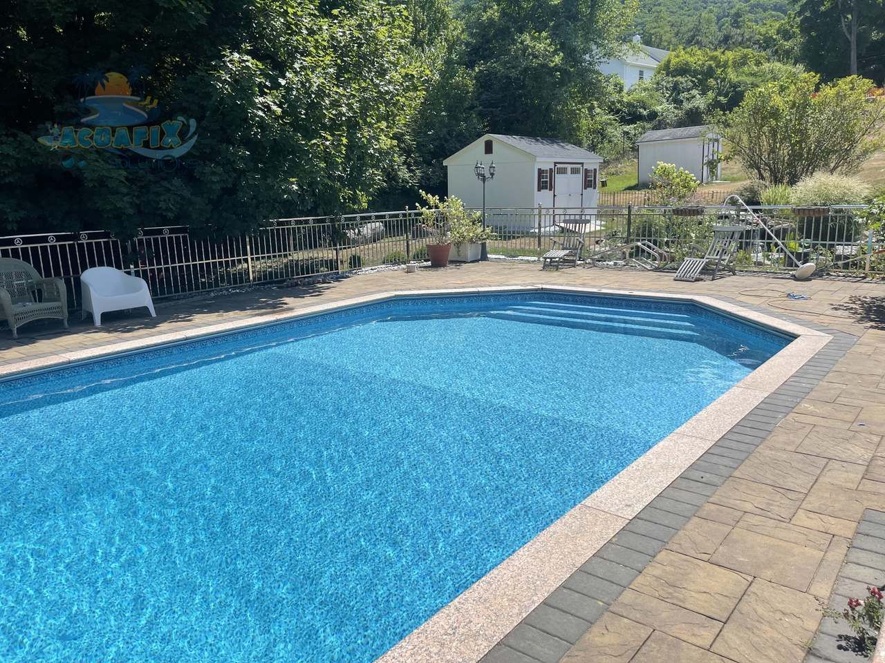 Backyard swimming pool with blue water, brick patio, lounge chairs, and trees around it