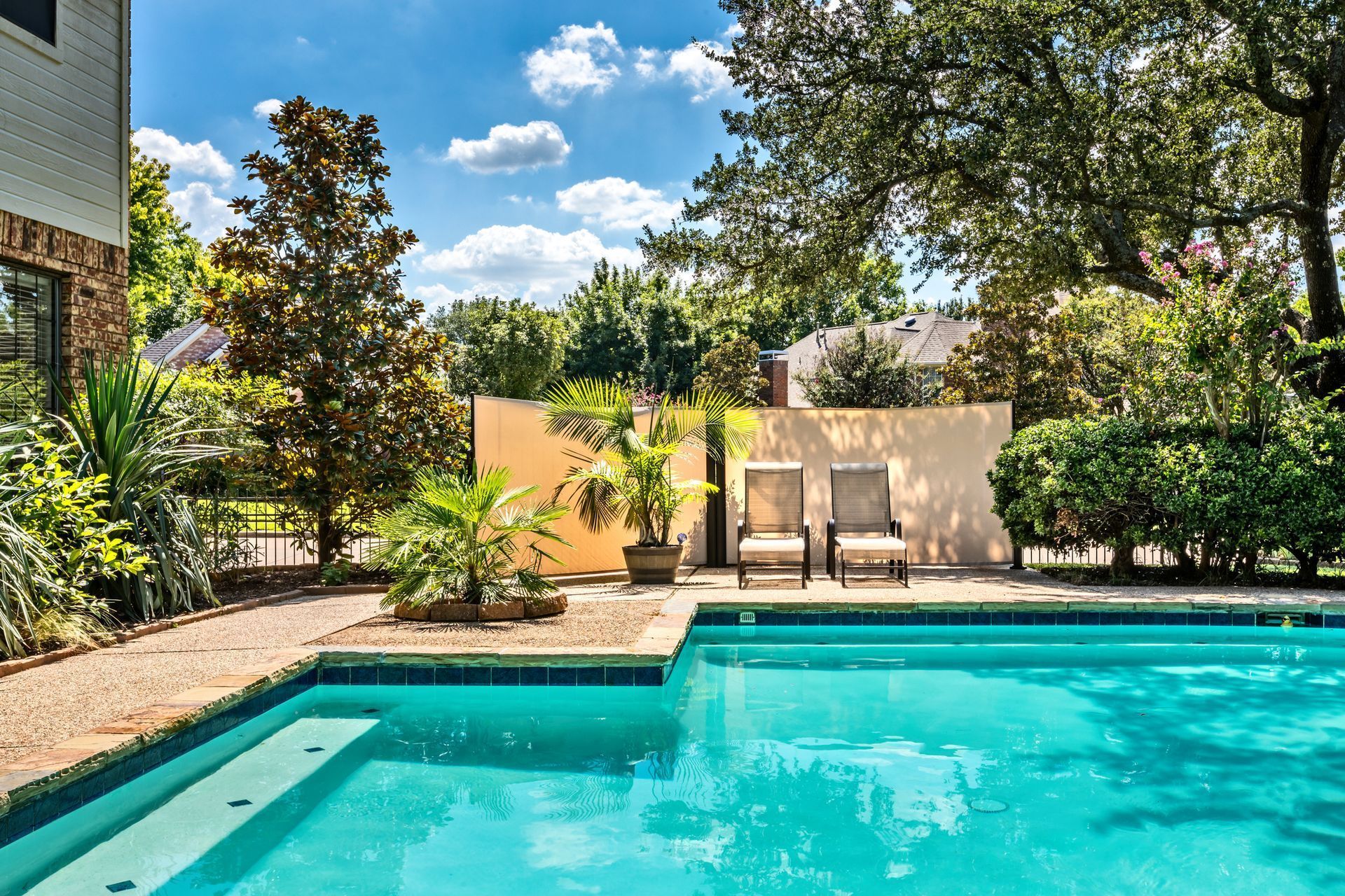 Backyard swimming pool with lounge chairs, trees, and a bright blue sky