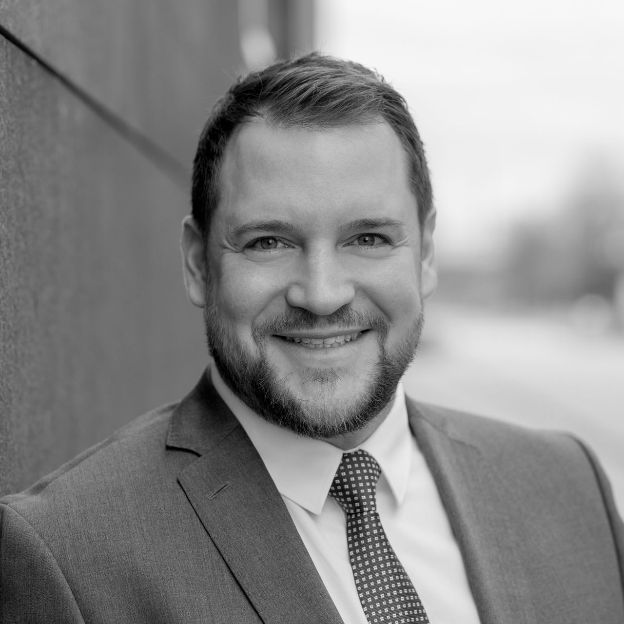 Auf einem Schwarzweißfoto lächelt ein Mann in Anzug und Krawatte.