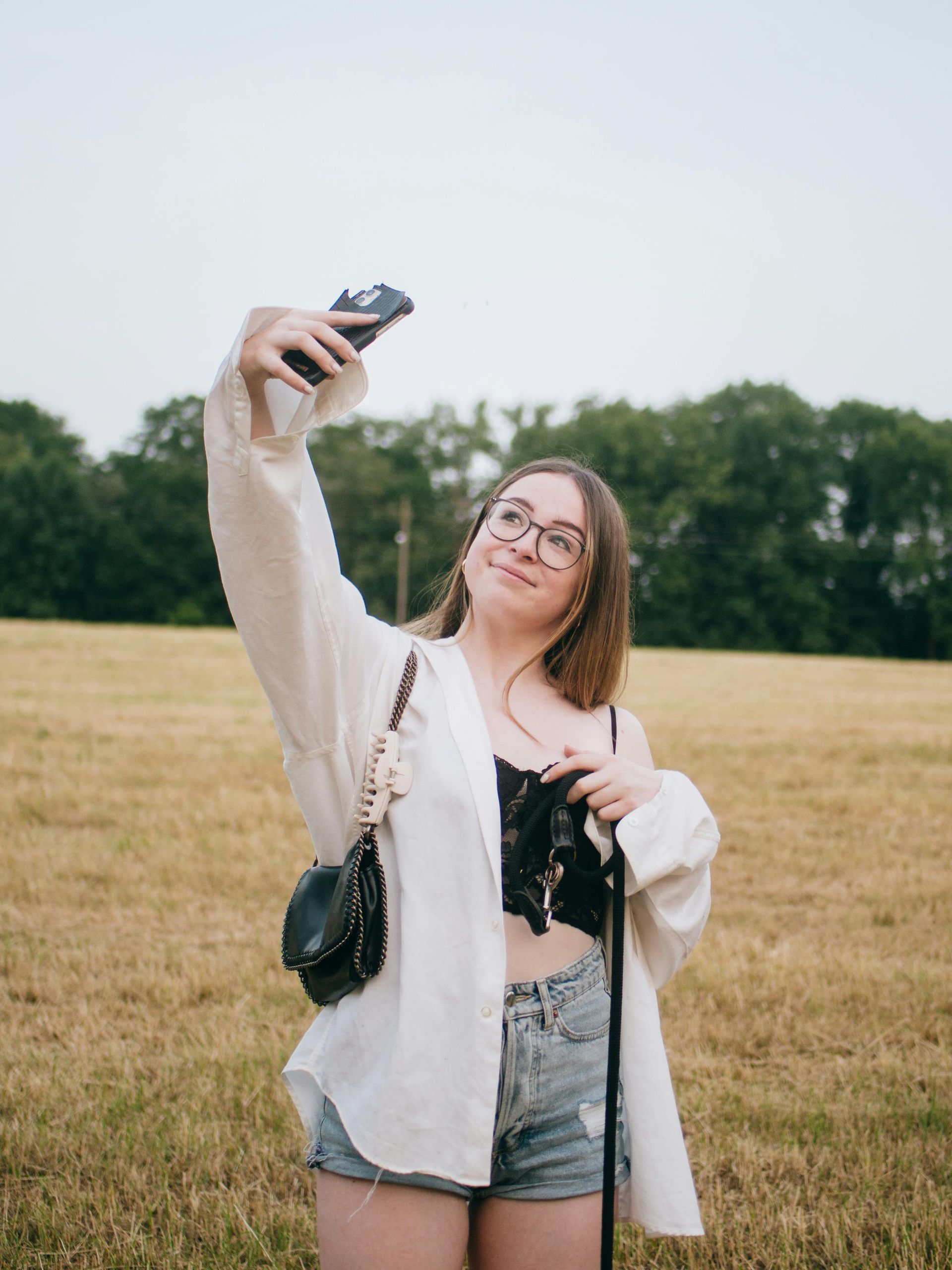 A woman is taking a selfie in a field with a camera.