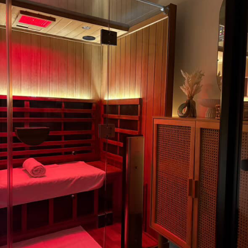 Woman in bikini and shirtless man sitting in sauna, illuminated by blue light.