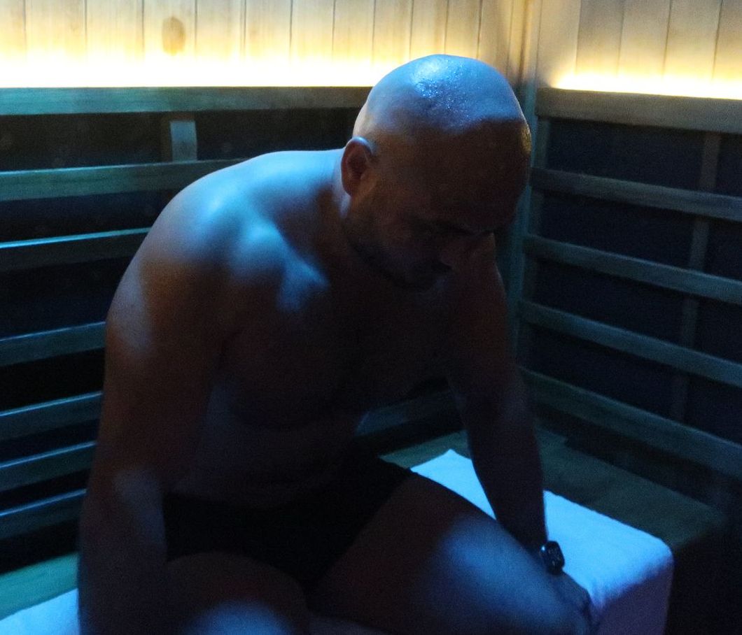 Woman in black bikini seated cross-legged in a sauna, with blue and amber lighting.