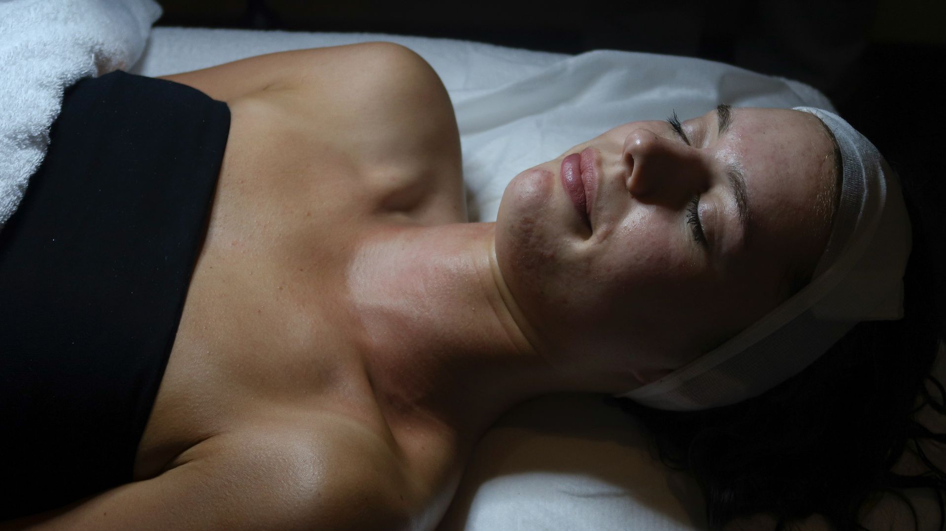 Woman in black bikini seated cross-legged in a sauna, with blue and amber lighting.