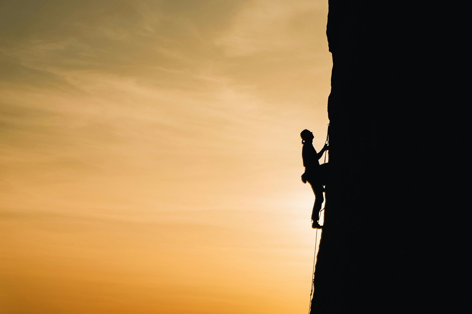 A silhouette of a person climbing a rock wall at sunset.