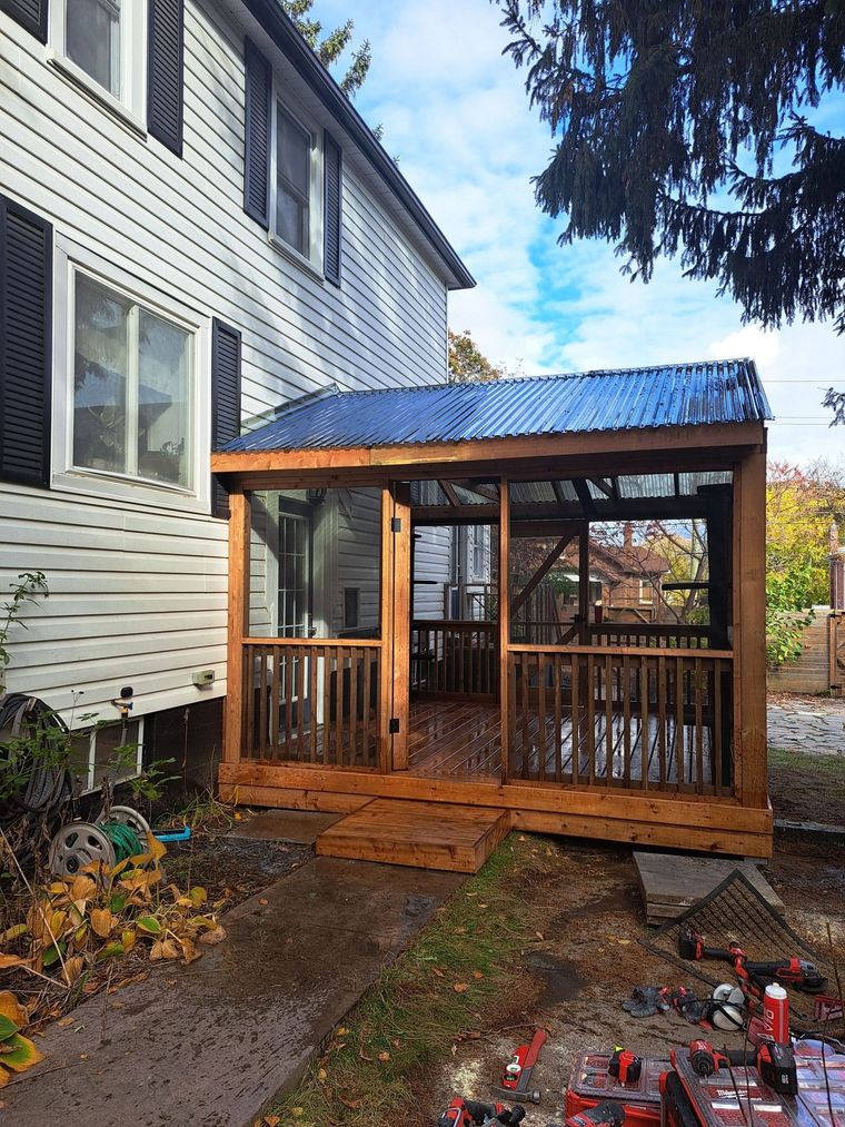 Wooden backyard gazebo with snow-dusted roof beside a house and stone patio in a garden.