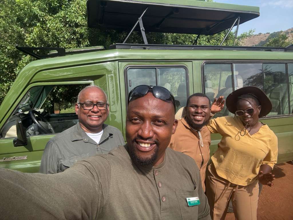Safari guests taking a group selfie next to an open-top safari vehicle