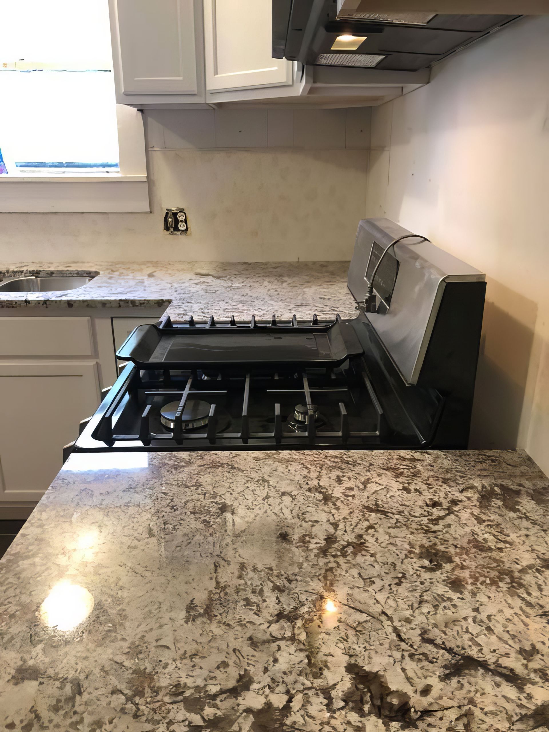 Modern kitchen with granite counters and a gas stove, one burner grate lifted upright.