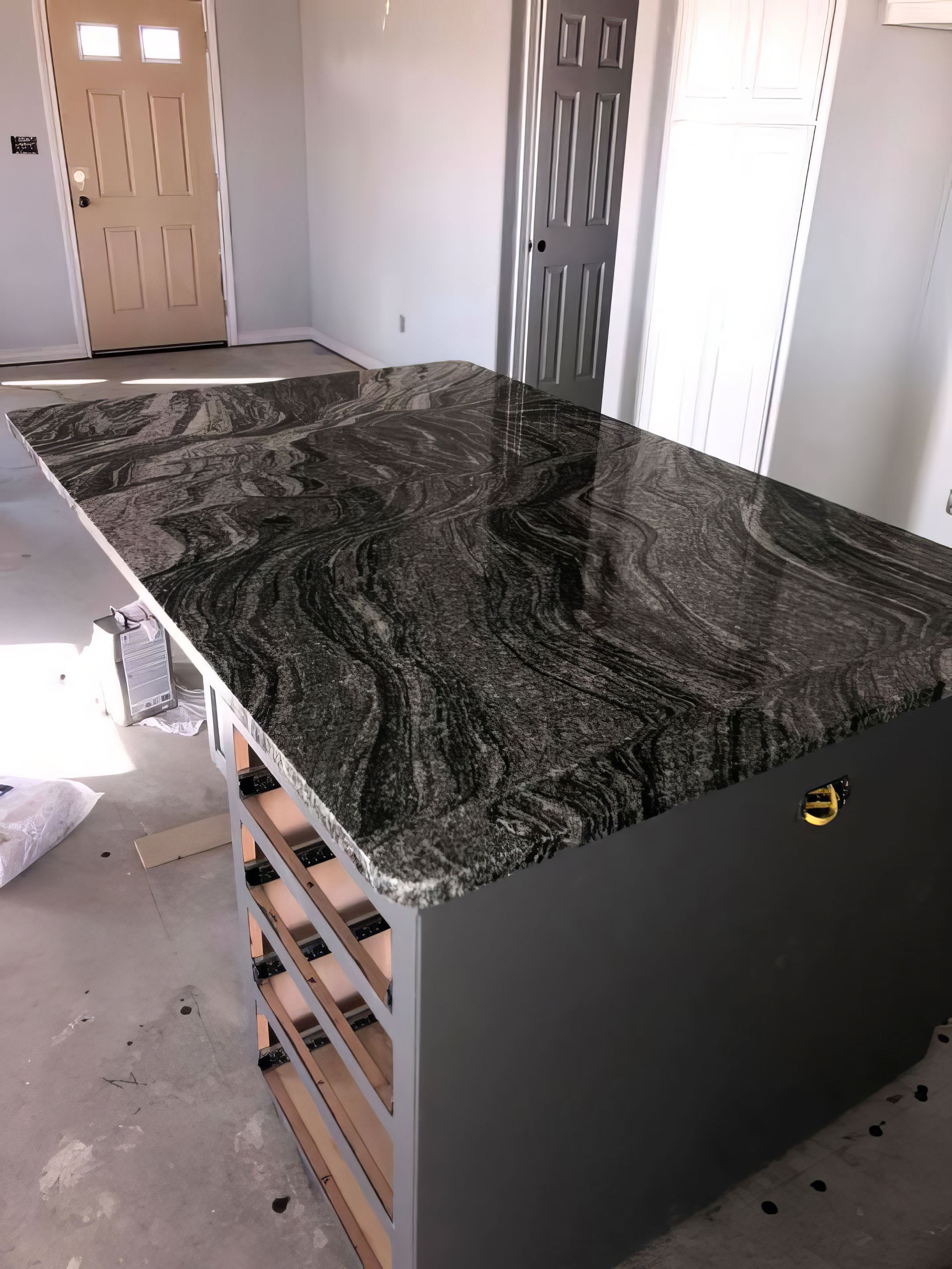 Kitchen island with dark granite countertop and black cabinet base in an unfinished room