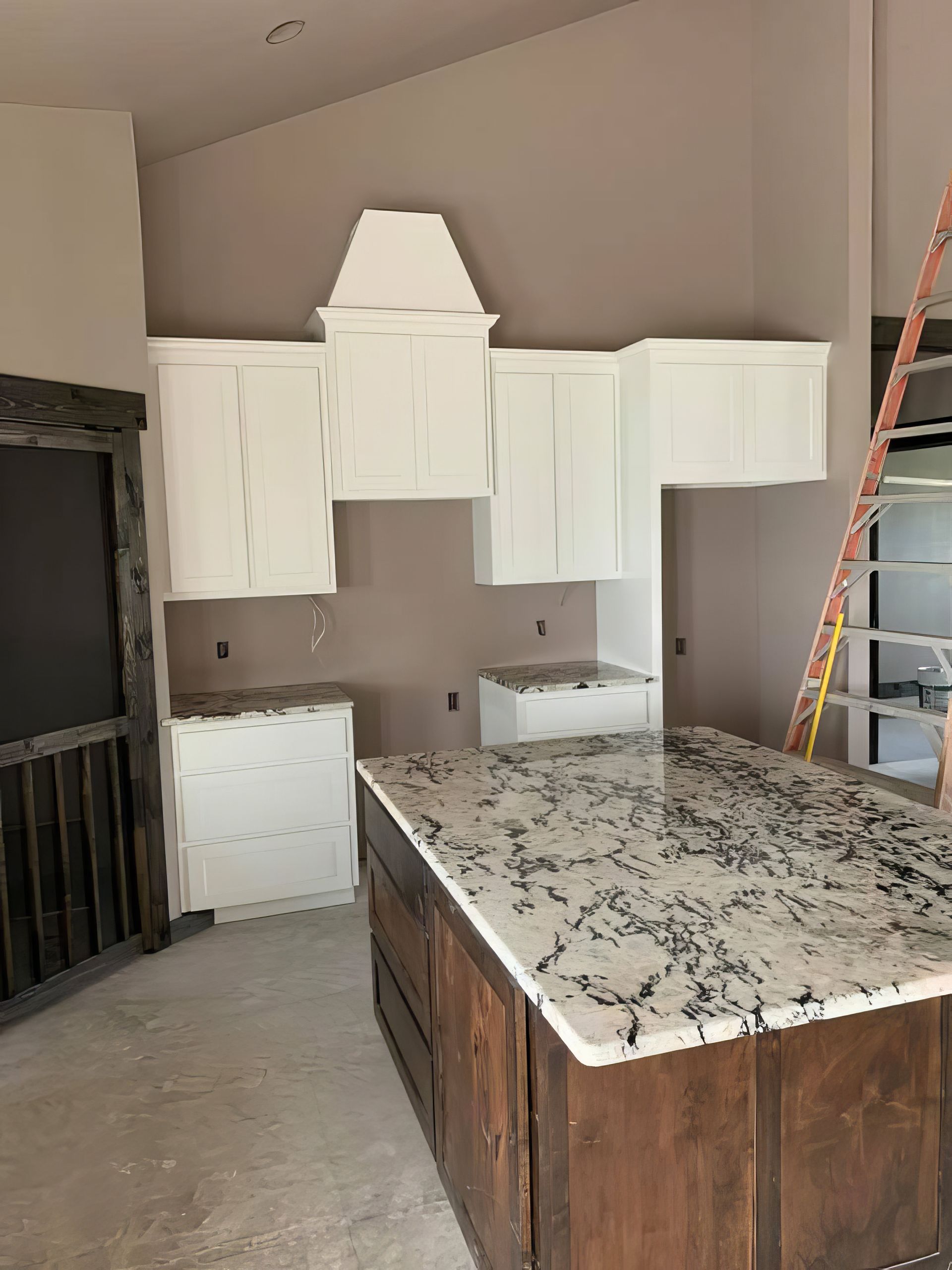 Kitchen under renovation with white cabinets, granite island, and a ladder against the wall
