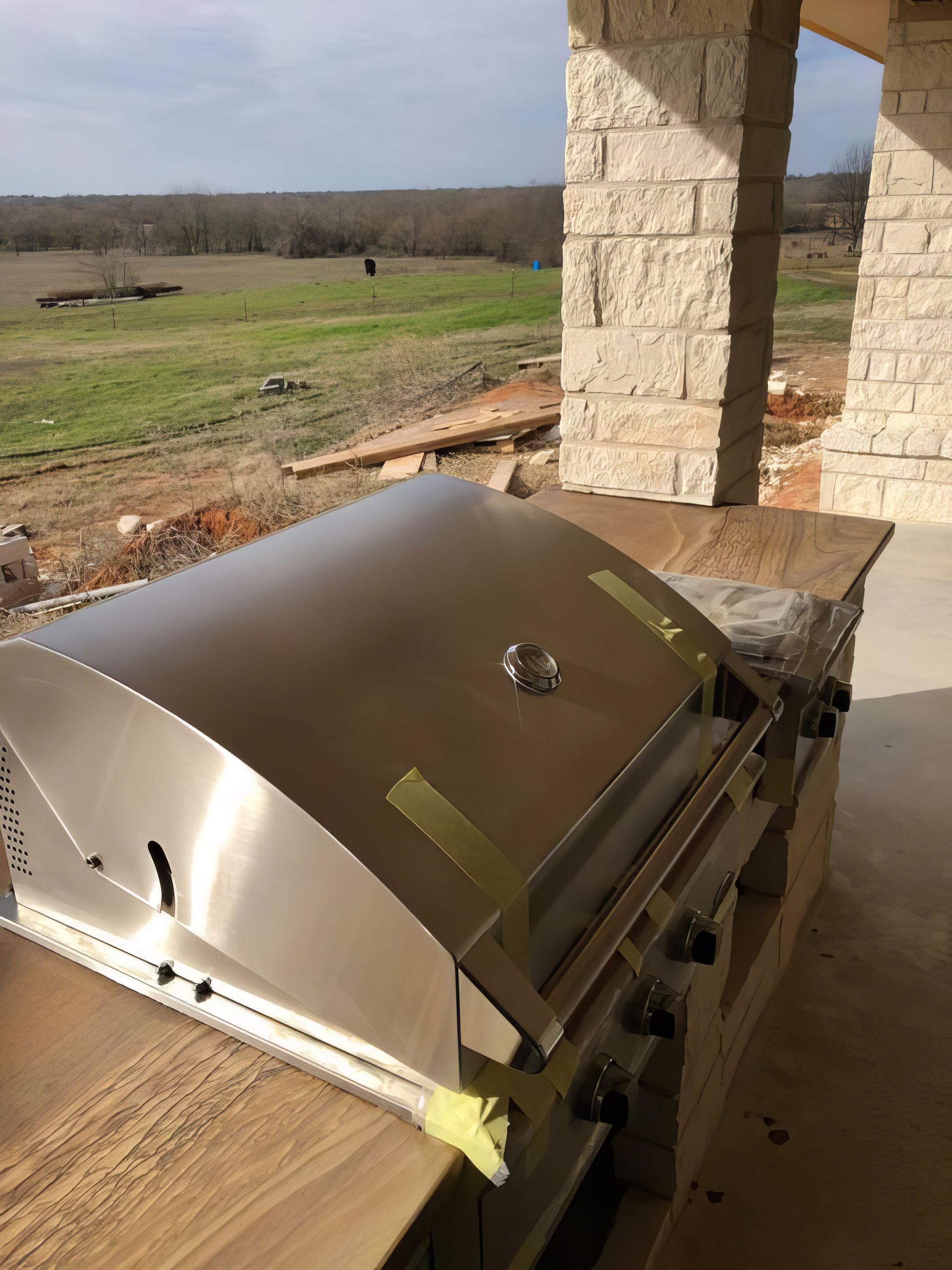 Stainless steel grill on a wooden deck overlooking a grassy field and stone patio pillar