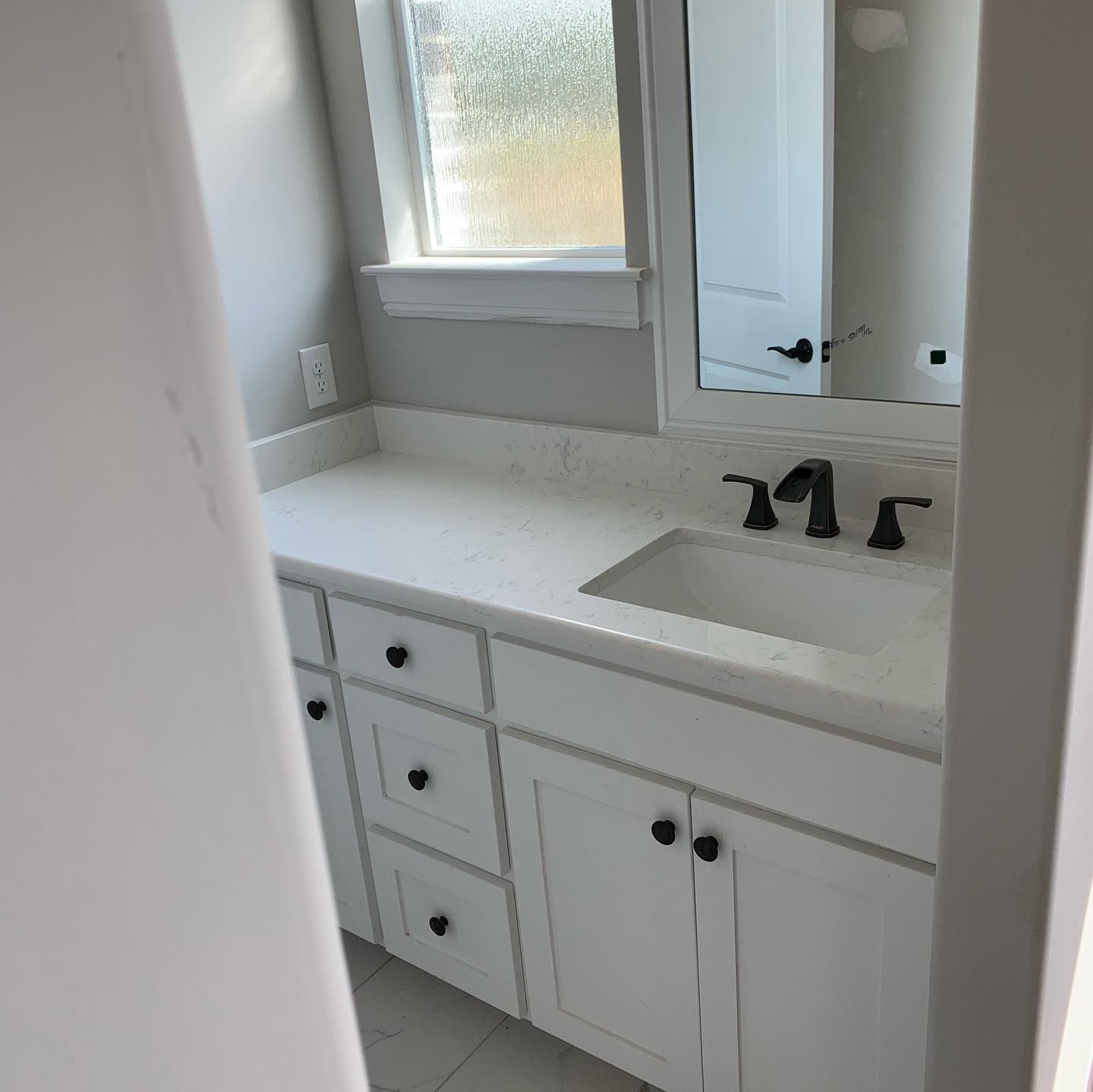 White bathroom vanity with sink, black faucet, mirror, and frosted window in a small bright room