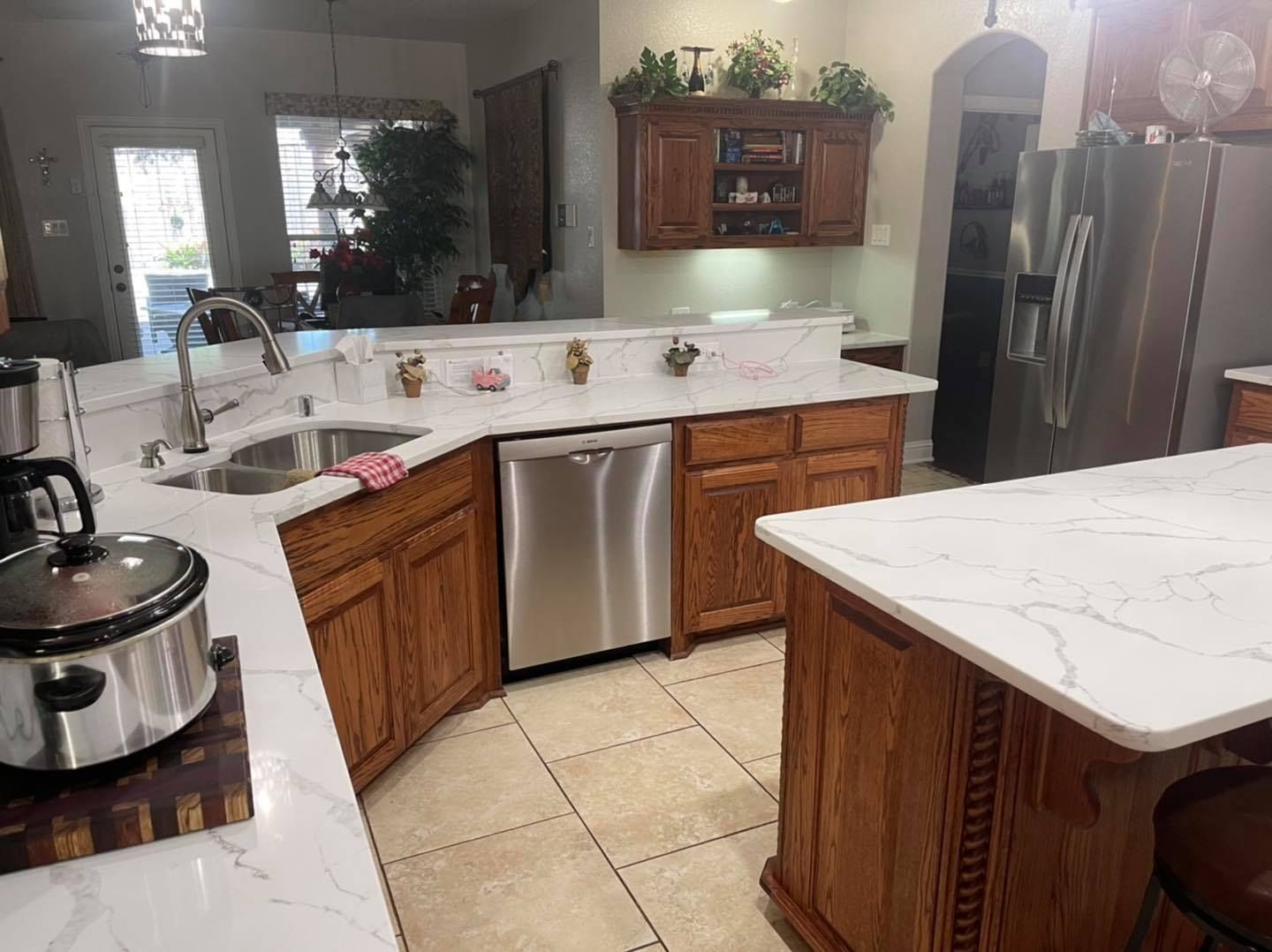 Bright kitchen with marble countertops, wooden cabinets, stainless steel appliances, and tiled floor.