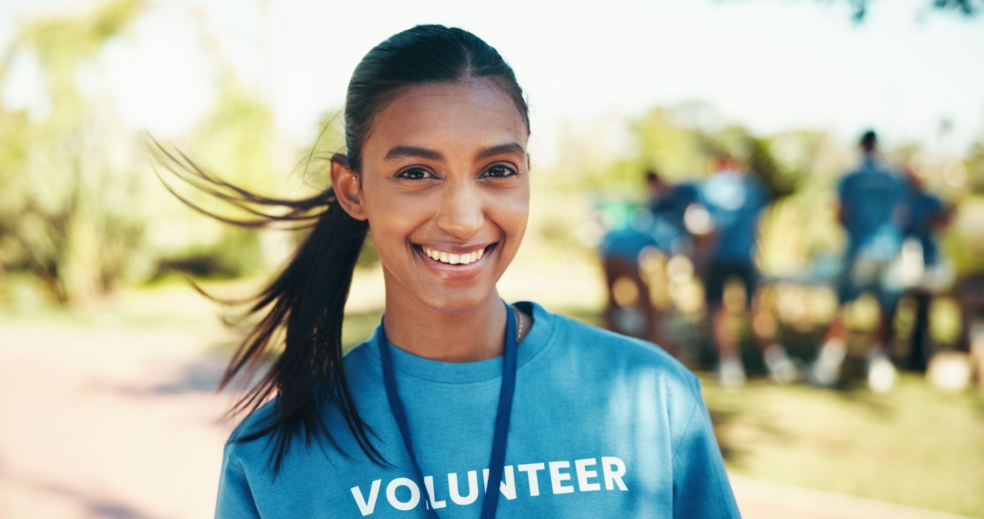 A young woman is wearing a blue volunteer shirt and smiling.