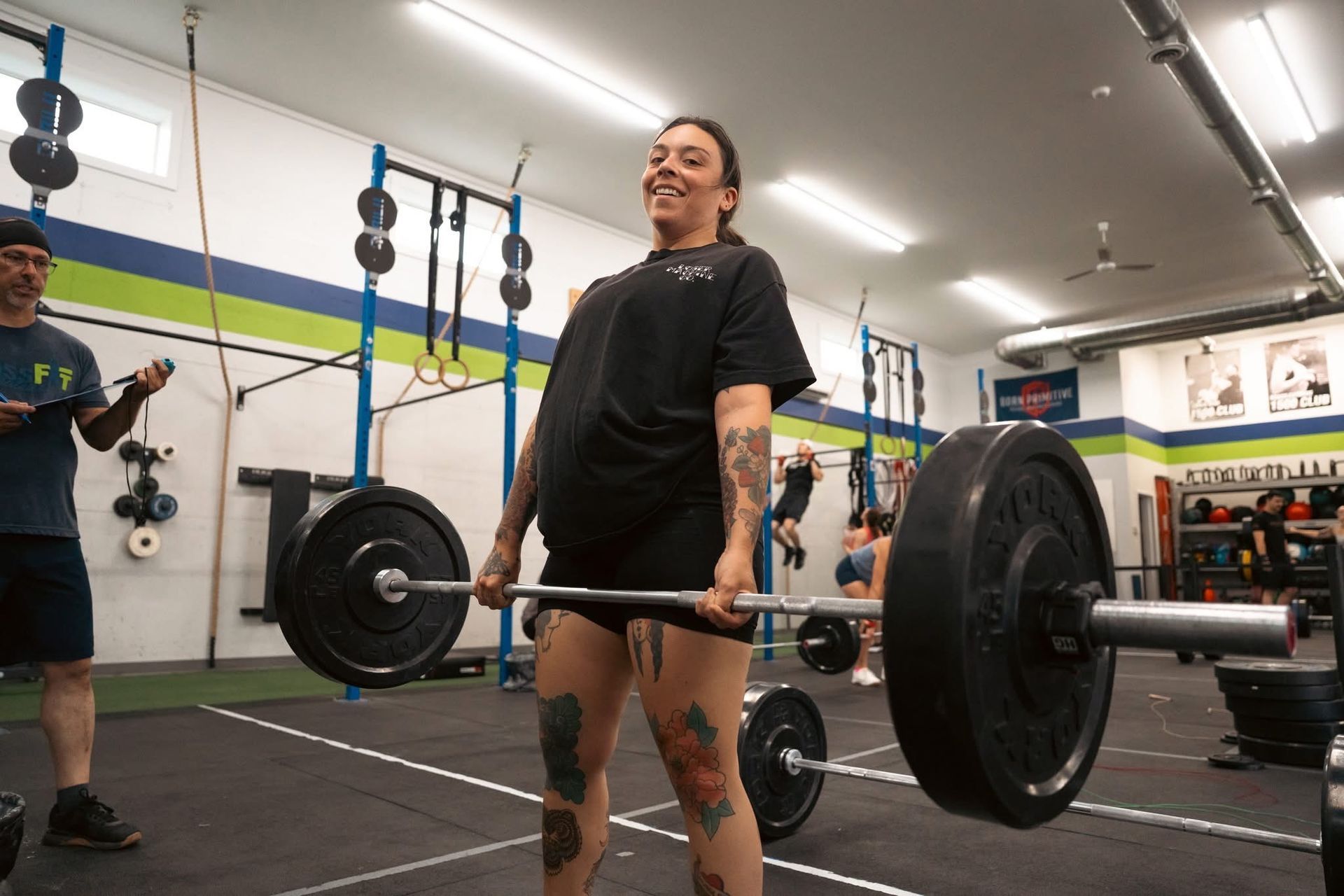 Two people exercising on rowing machines in a gym, with one man in the foreground smiling.