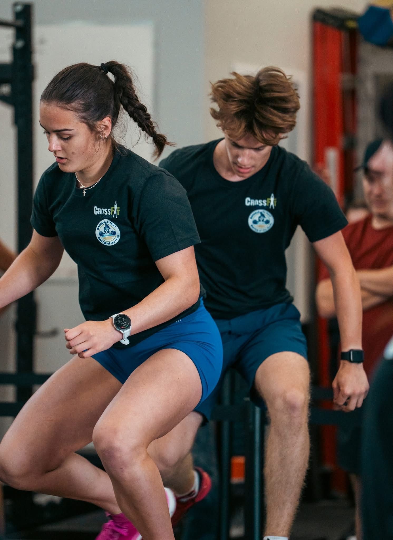 Two people talking in a gym, standing near exercise equipment and weight racks.