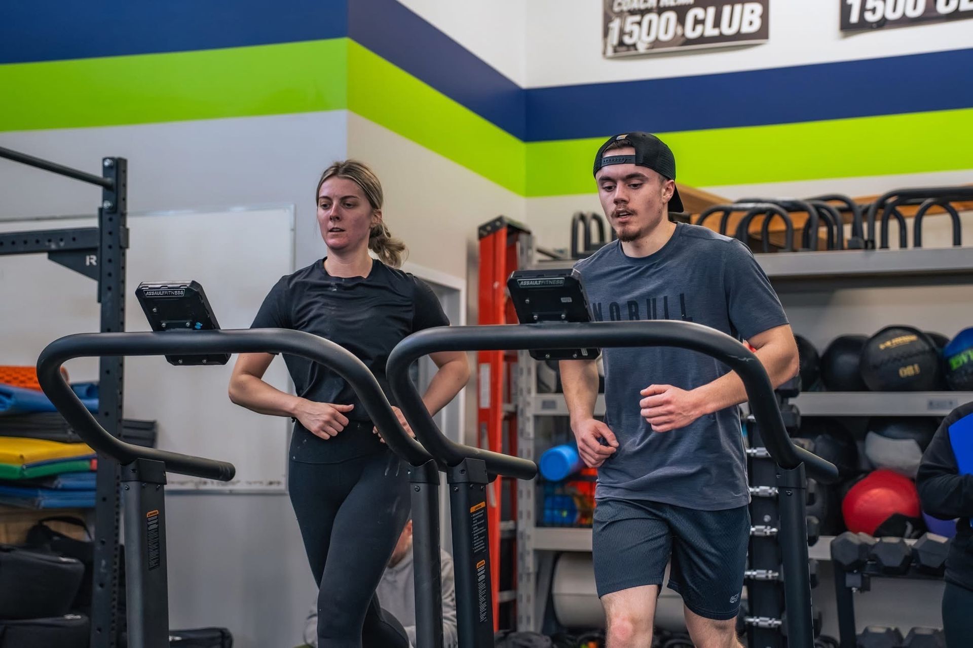 People working out on treadmills in a gym with weight equipment and green turf.
