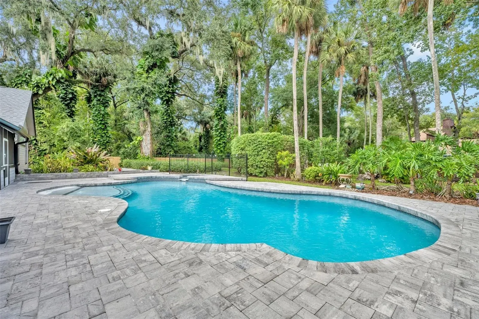 Backyard pool with blue water, stone patio, and lush trees and shrubs surrounding it