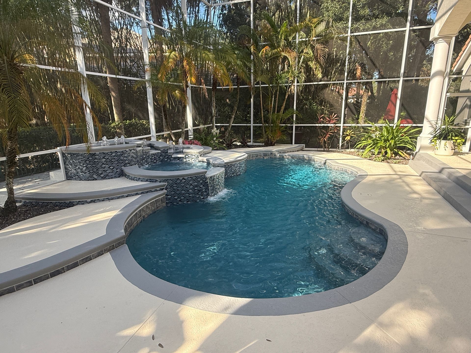 Backyard pool with a curved spa and light stone deck, surrounded by tropical landscaping