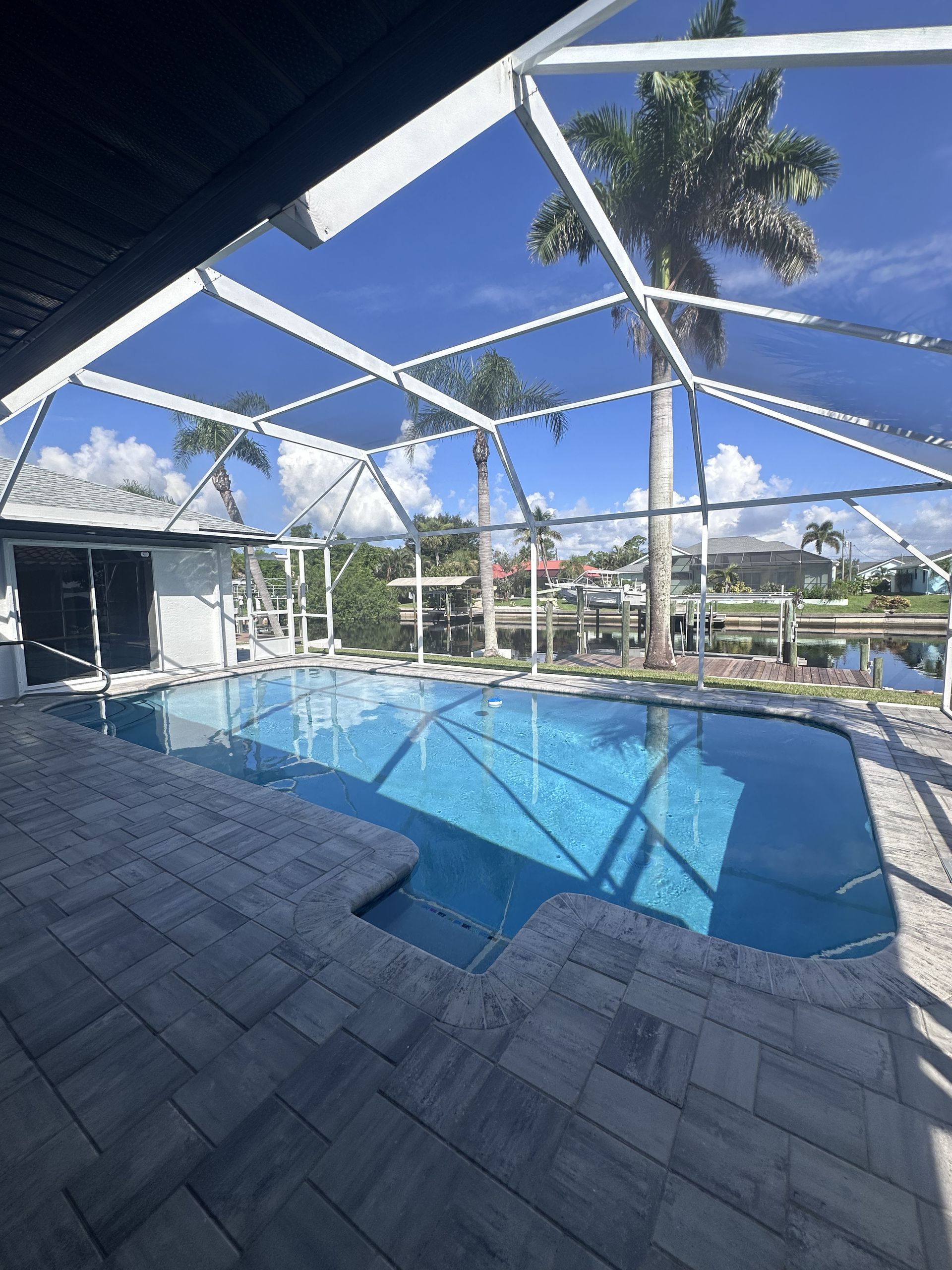 Screened outdoor pool with blue water, palm trees, and lounge chairs under a bright sky