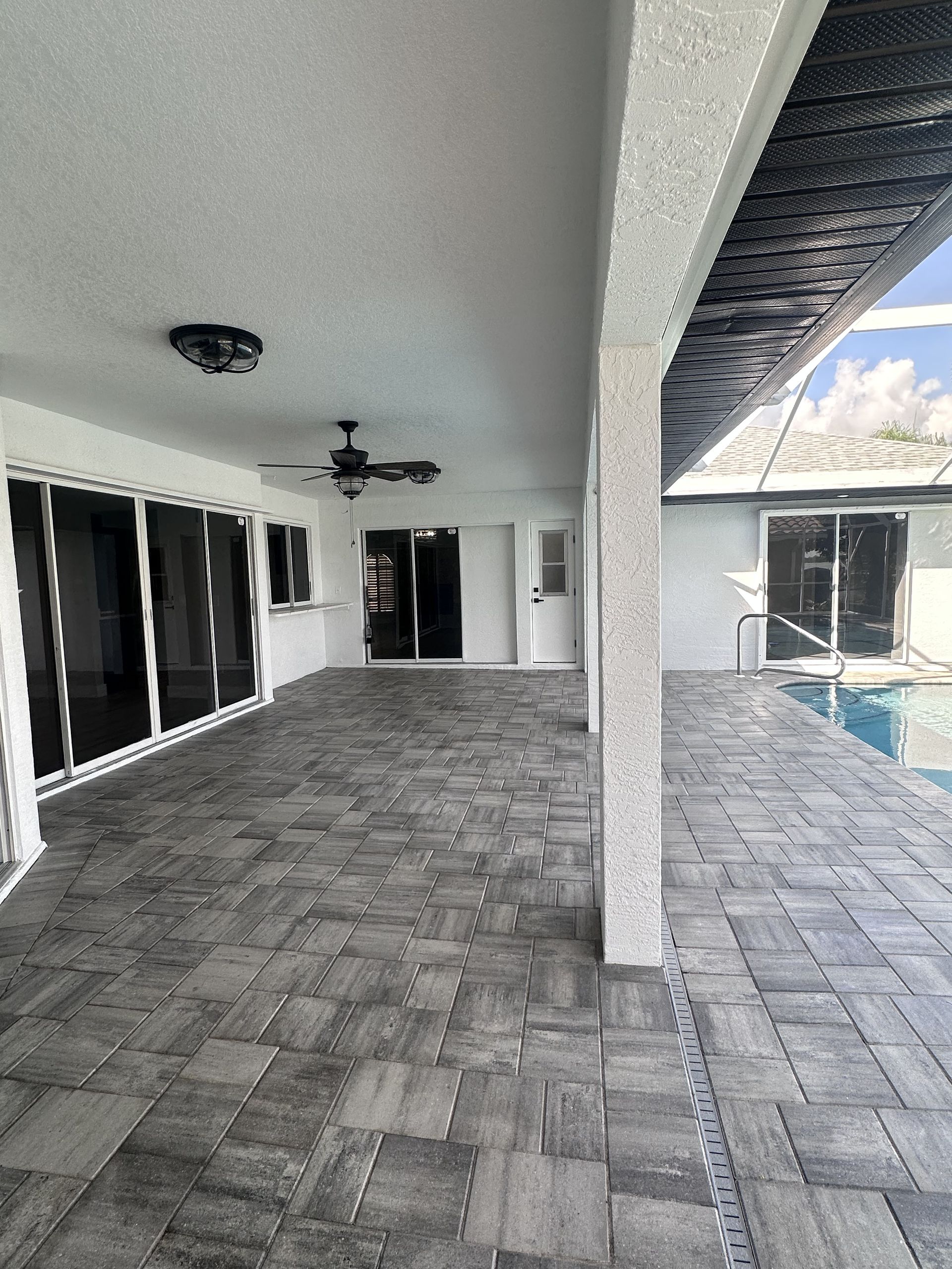Covered patio with gray pavers, white columns, sliding glass doors, and a ceiling fan.