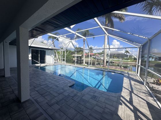 Screened-in backyard pool with blue water, patio pavers, and palm trees beyond the enclosure.