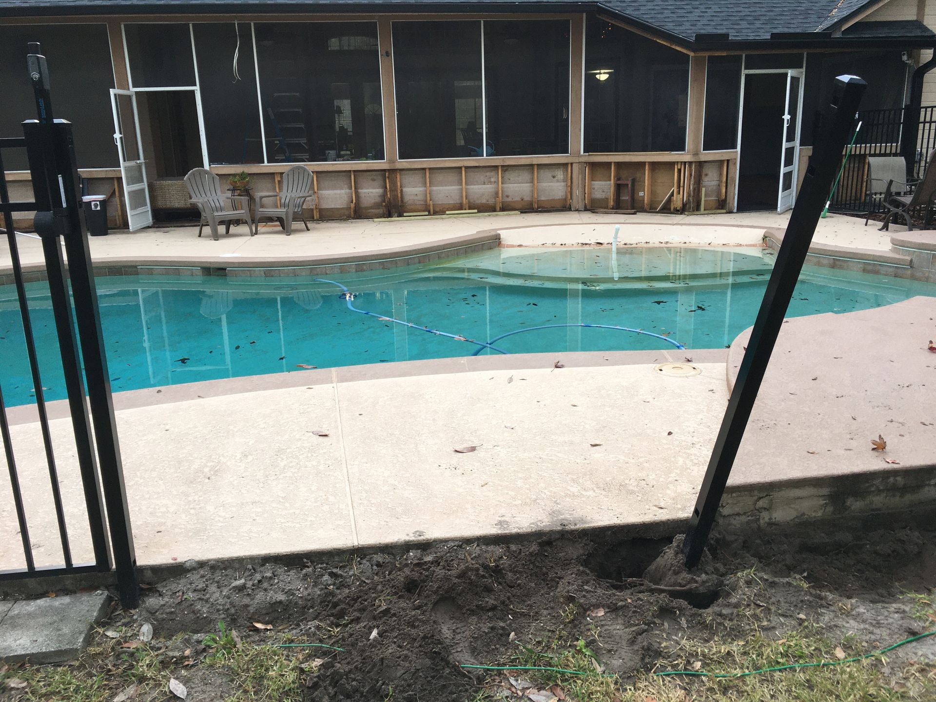 Backyard pool behind a screened patio with a wooden fence and beige deck.