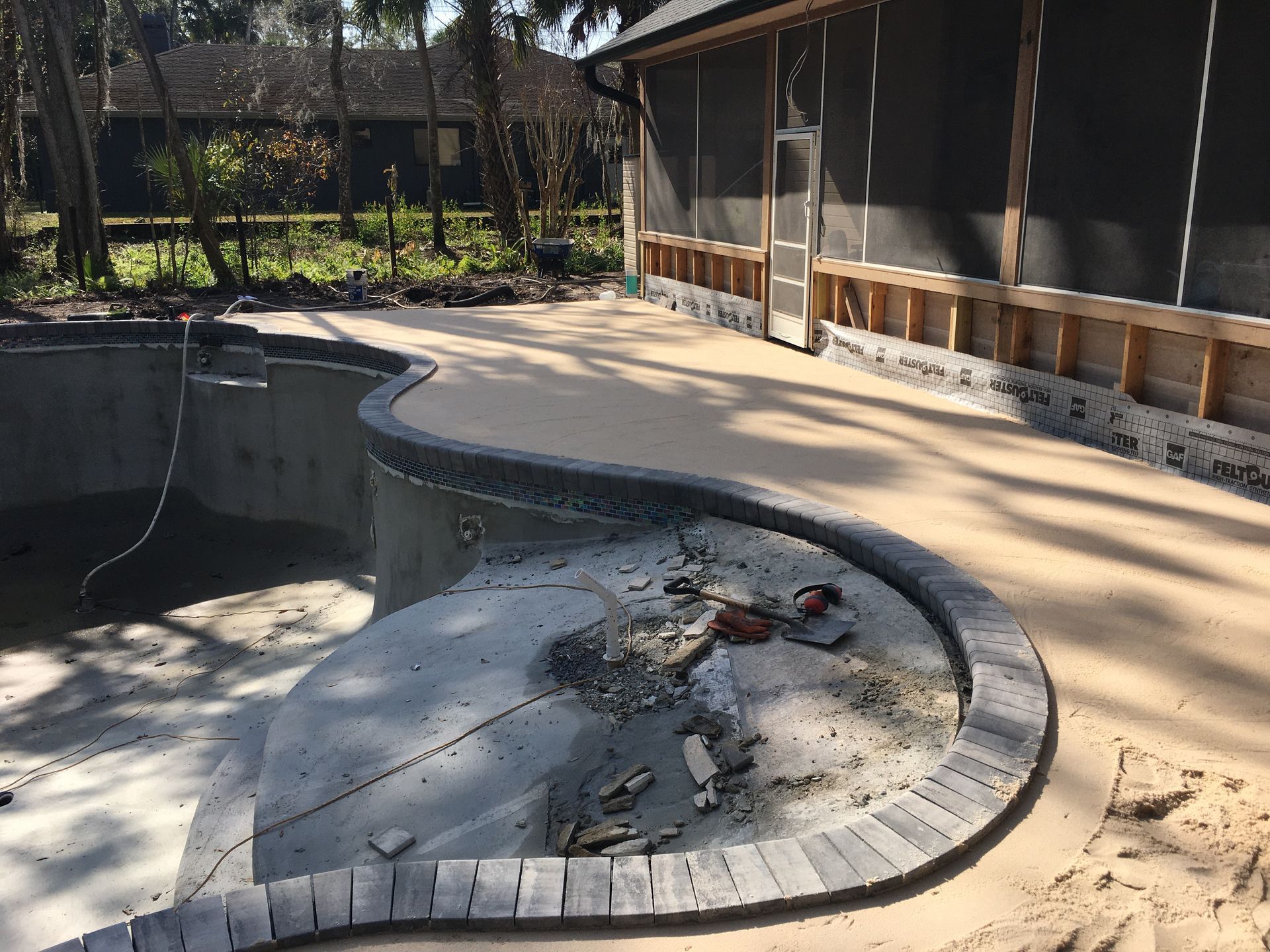Empty, partially drained backyard pool with cracked concrete and debris, beside a house and patio.
