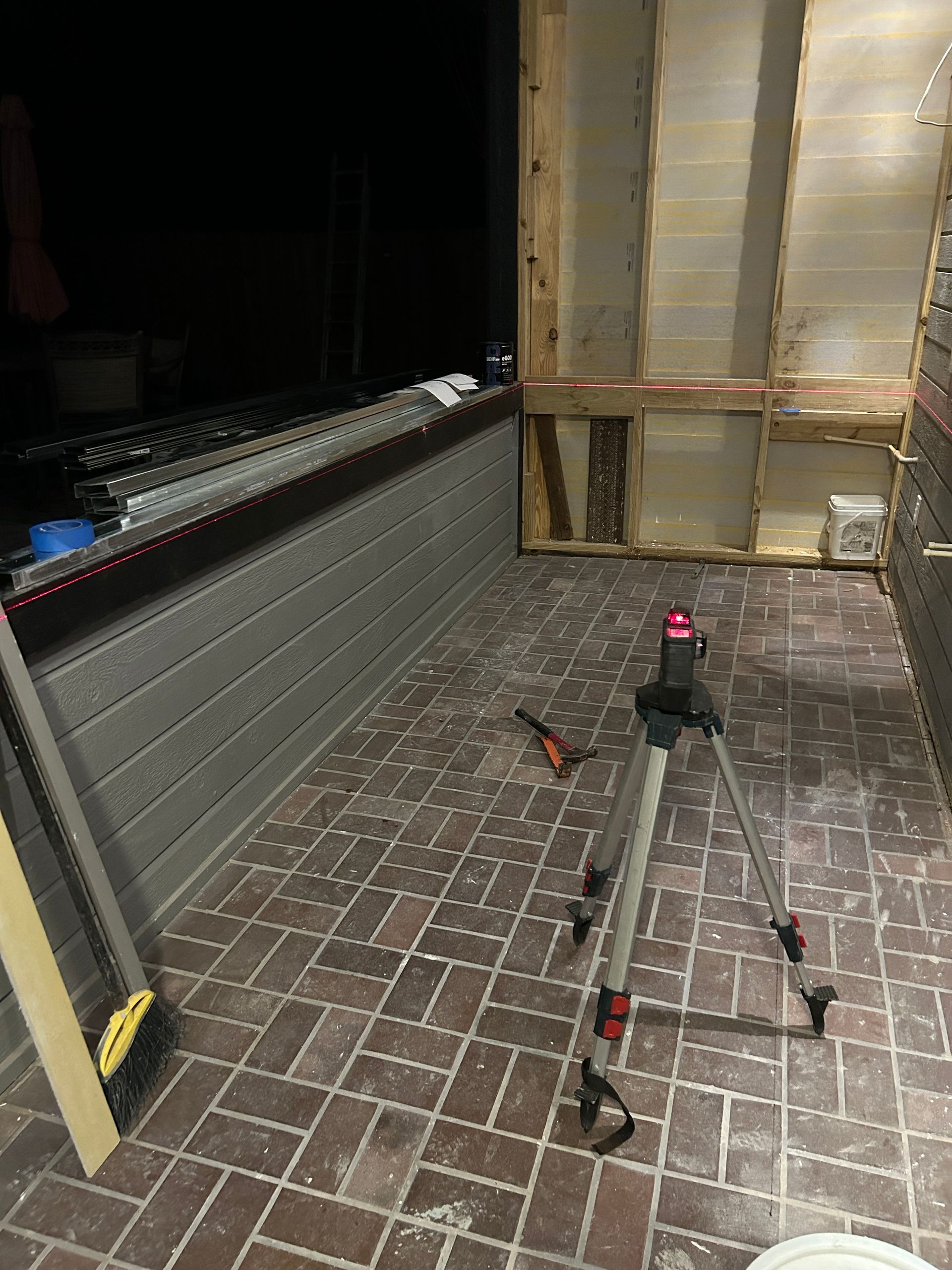 Indoor construction area with brick floor, scattered tools, and a partially covered wall section