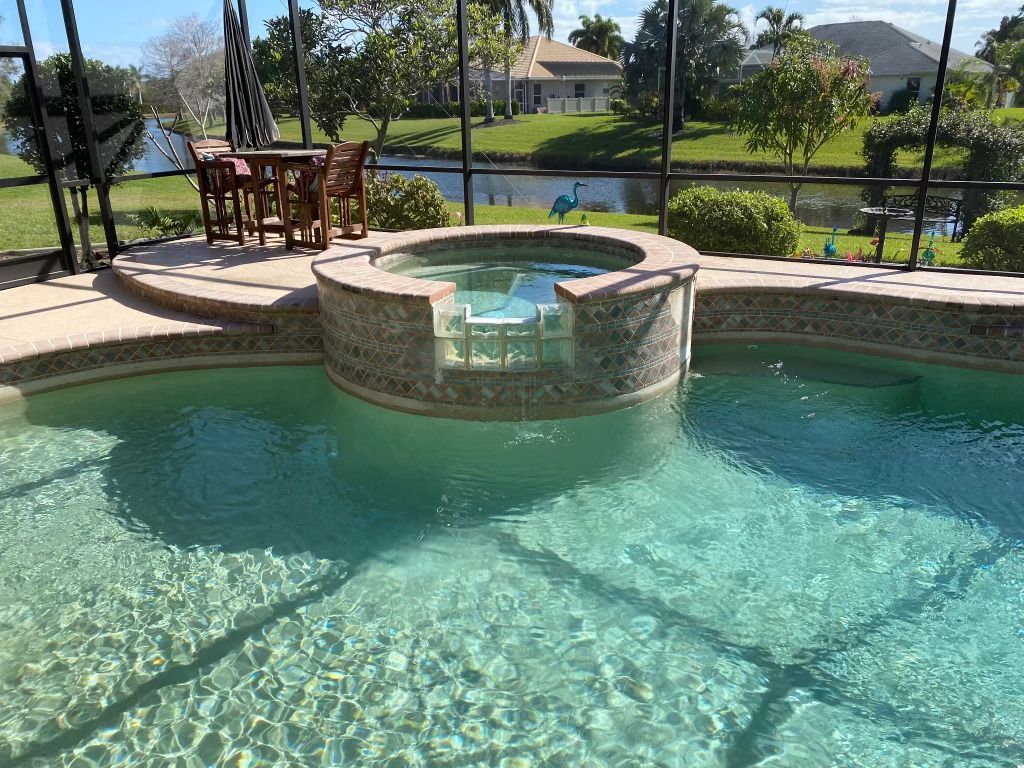 Backyard pool with a round stone hot tub, patio table, and mountain view through a fence