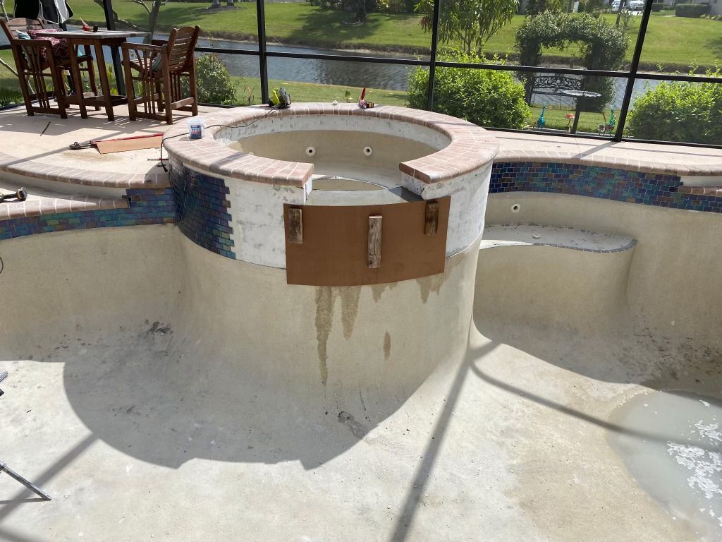 Empty outdoor pool with a built-in hot tub and a wooden cover, shown in bright sunlight.