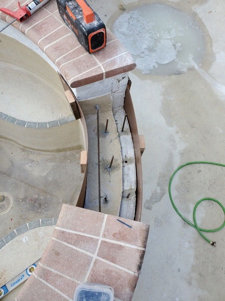 Curved brick walkway under construction with a small orange tool on top and a green hose on concrete nearby
