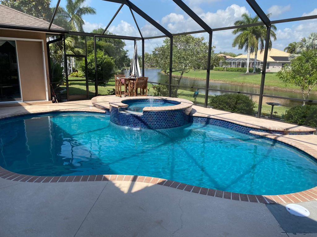 Backyard pool with blue water and a round spa under a screened patio, overlooking a lake