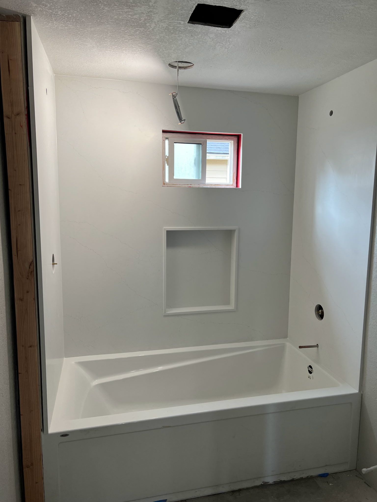 Bathroom with white tub, niche, and window; unfinished walls and ceiling.