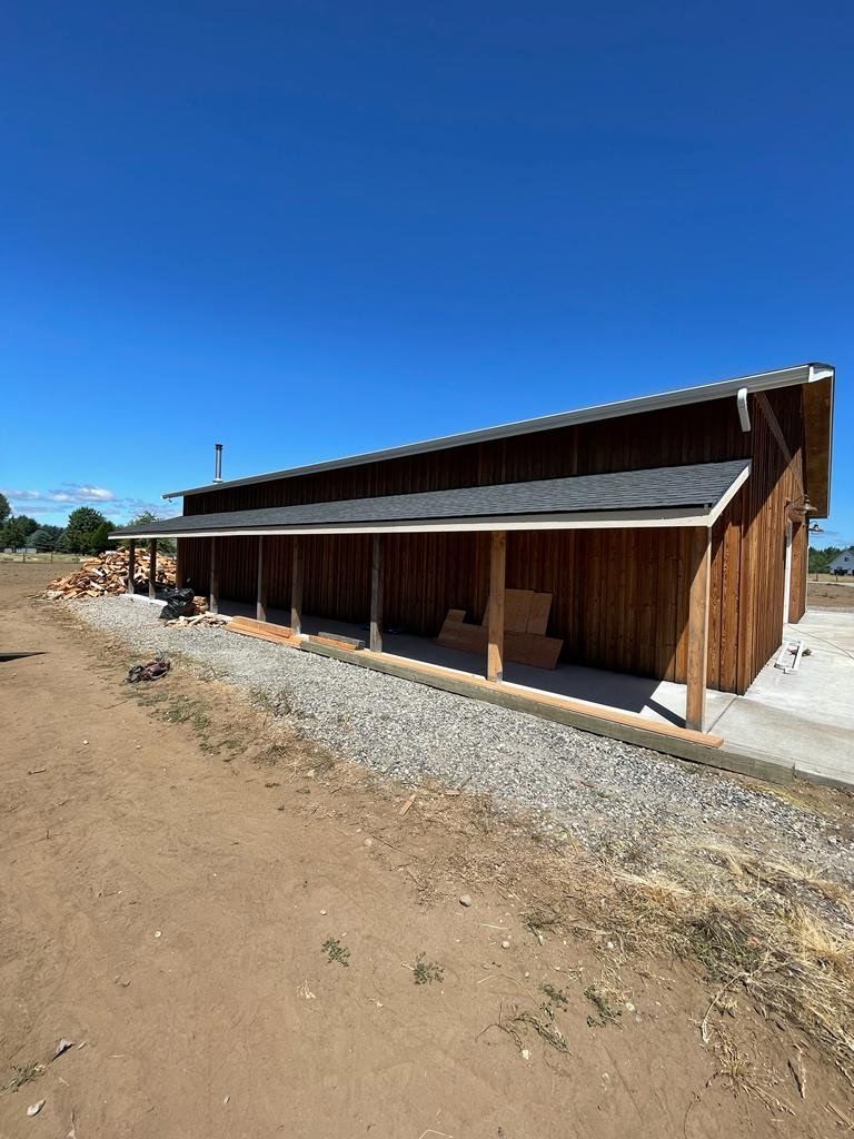 Wood-sided building with covered porch, gravel walkway, and blue sky.