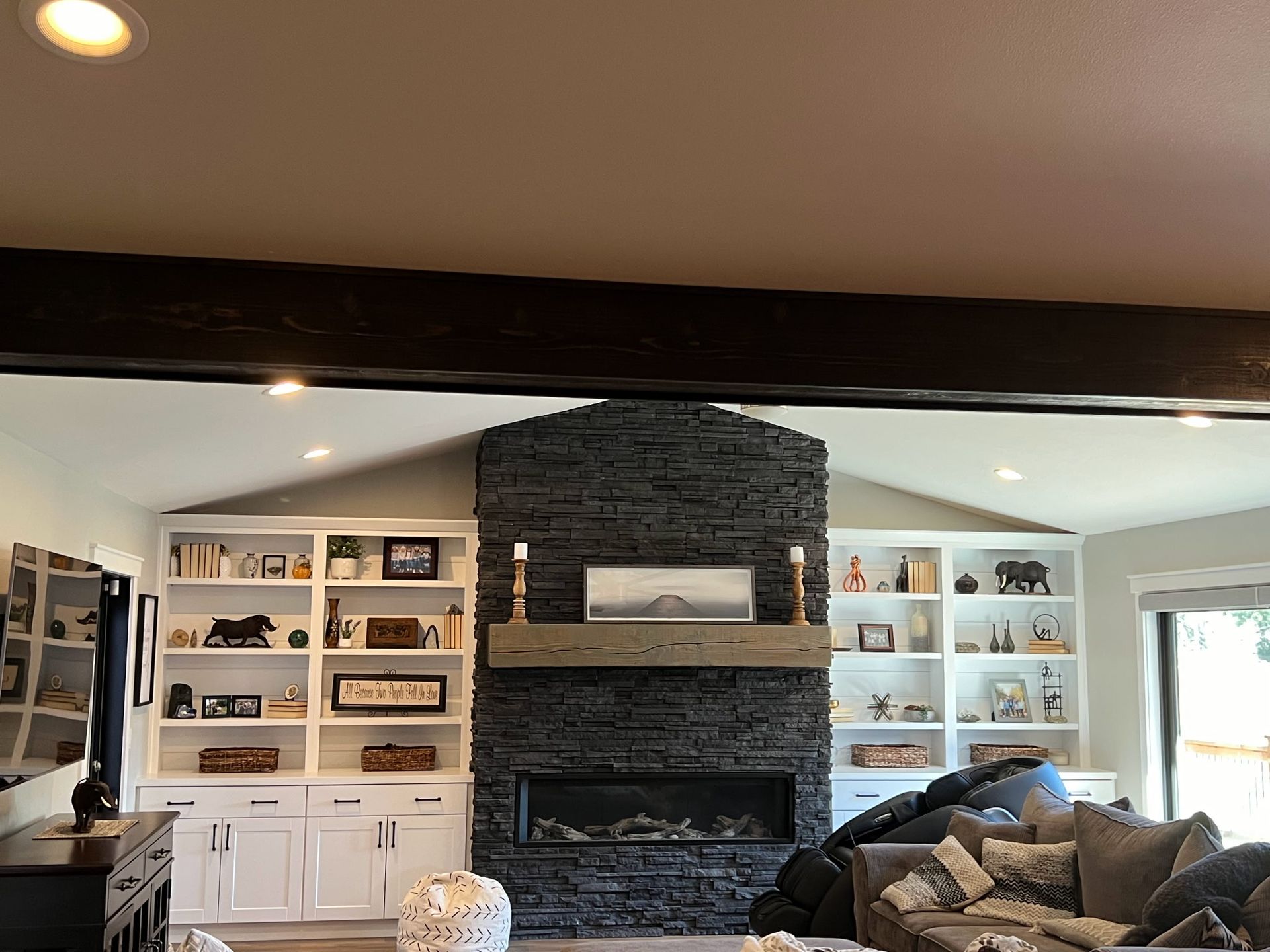 Living room with fireplace, bookshelves, and dark stone surround. A dark wood beam is above the structure.
