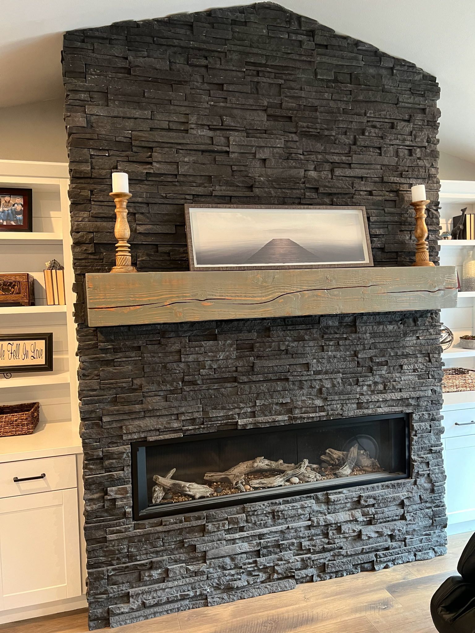 Newly built fireplace with dark stone facade, wooden mantle, candles, and built-in fireplace.