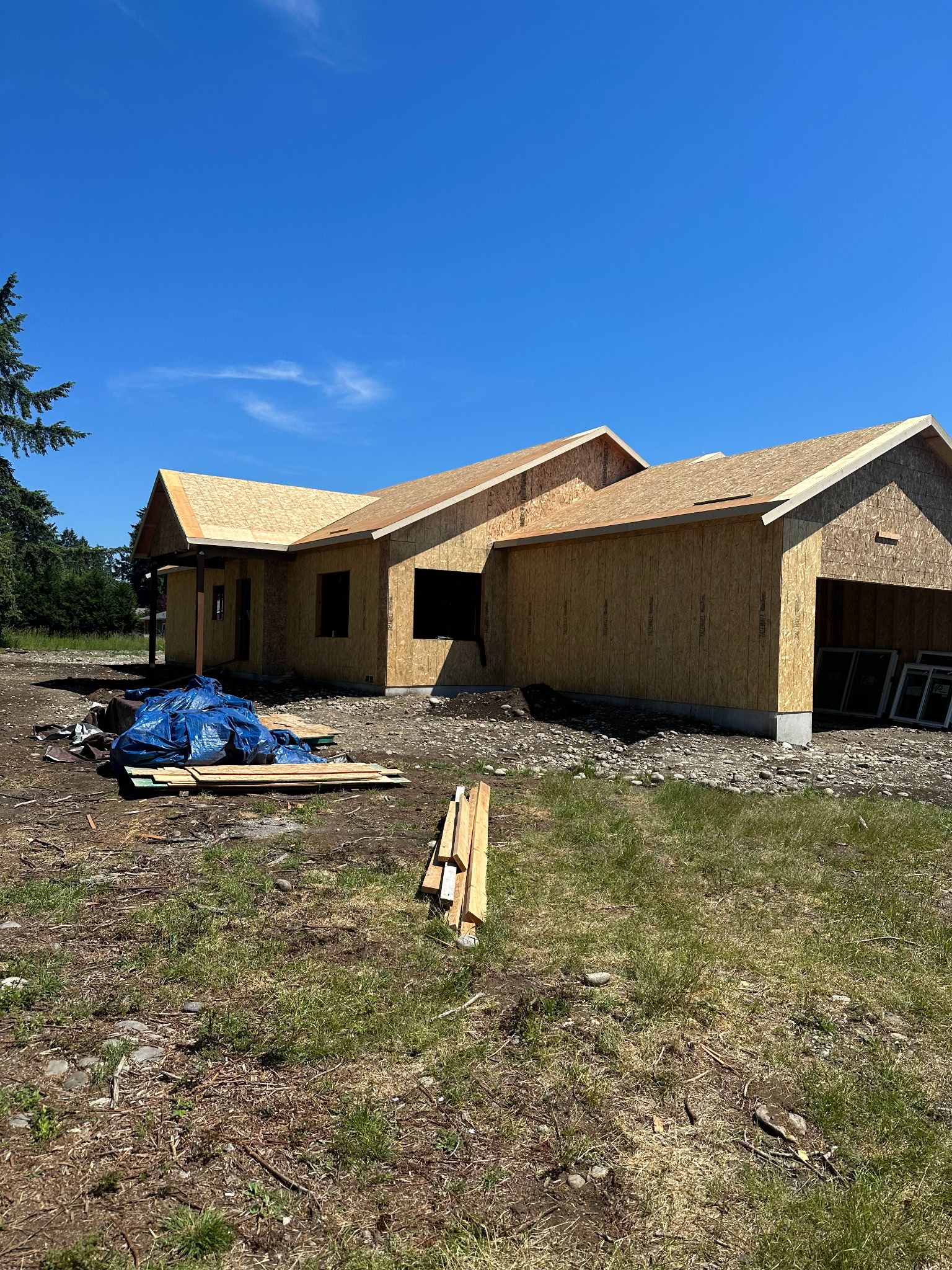 A new house under construction with exposed wooden framework, blue tarp, and clear blue sky.