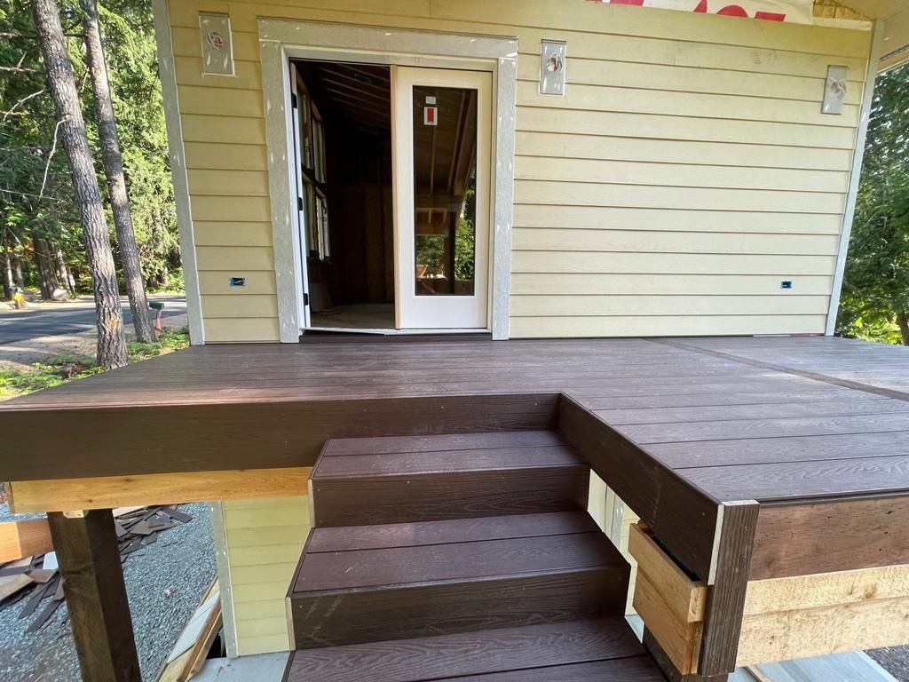 Exterior of a building under construction, featuring a deck with stairs and a sliding glass door.