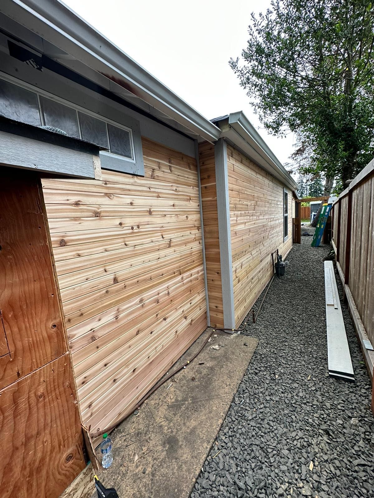 Exterior of a building with newly installed wooden siding. Gravel path along the side. Cloudy sky.