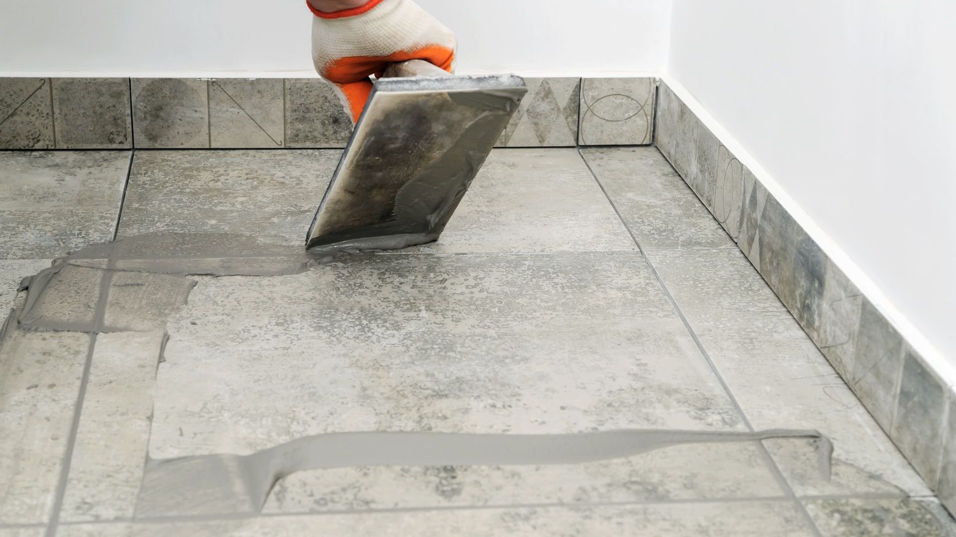 A person is laying tiles on a floor with a trowel.
