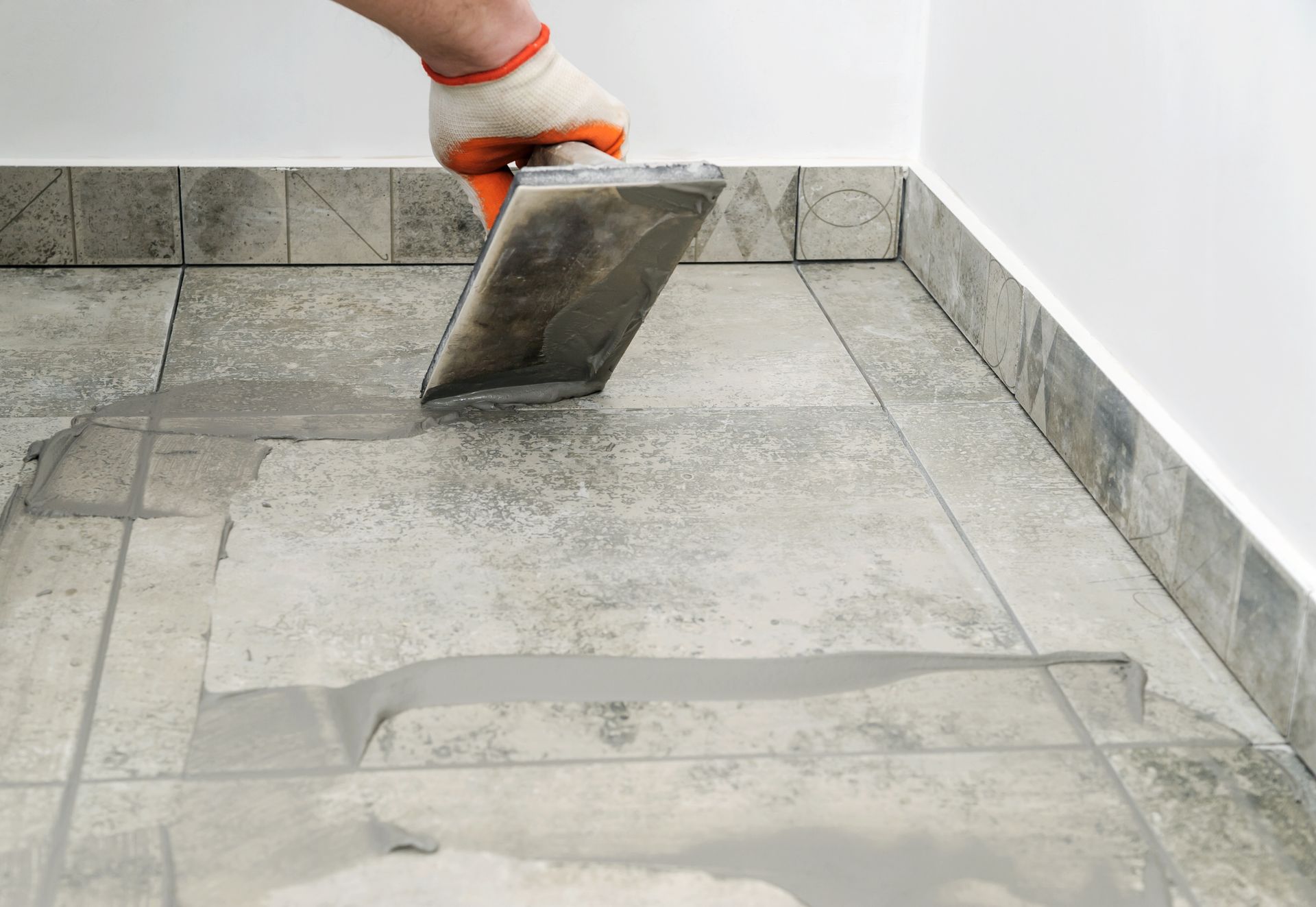 A person is using a trowel to spread cement on a tiled floor.