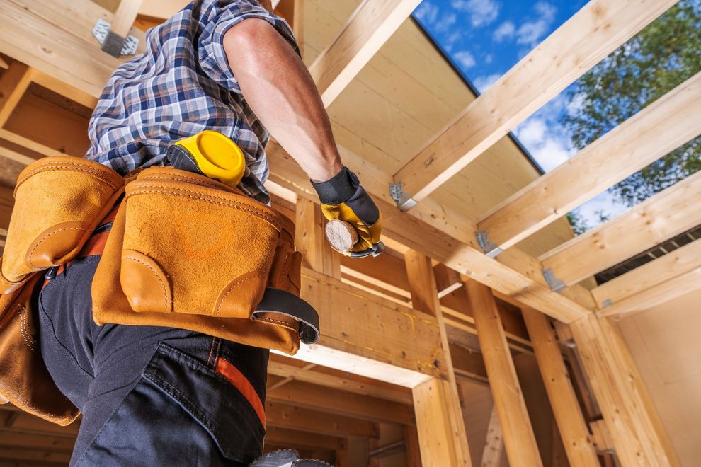 Construction worker nailing wooden beams in a framed house under construction