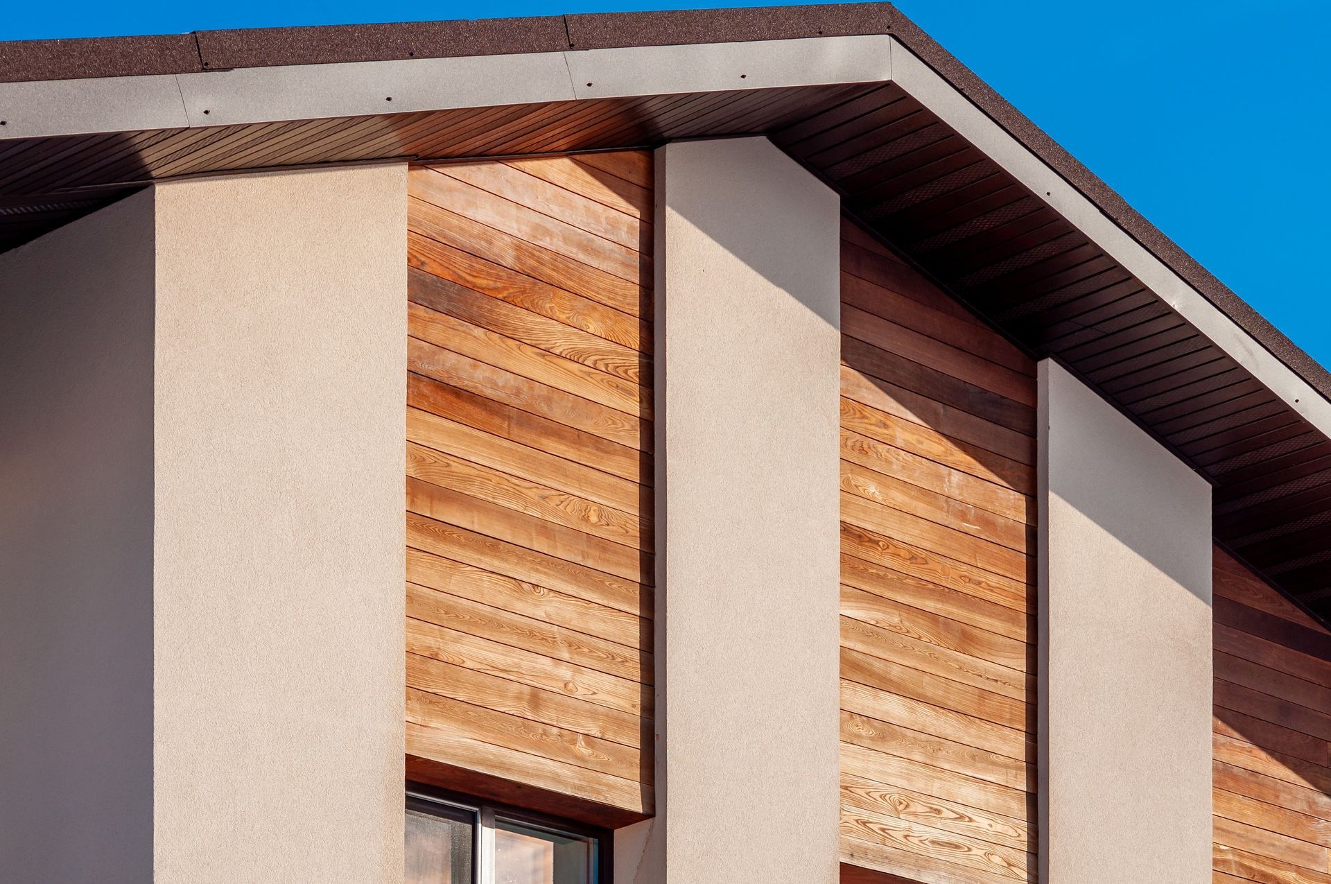 Modern building facade with beige walls, wood panel accents, and a flat roof against a blue sky