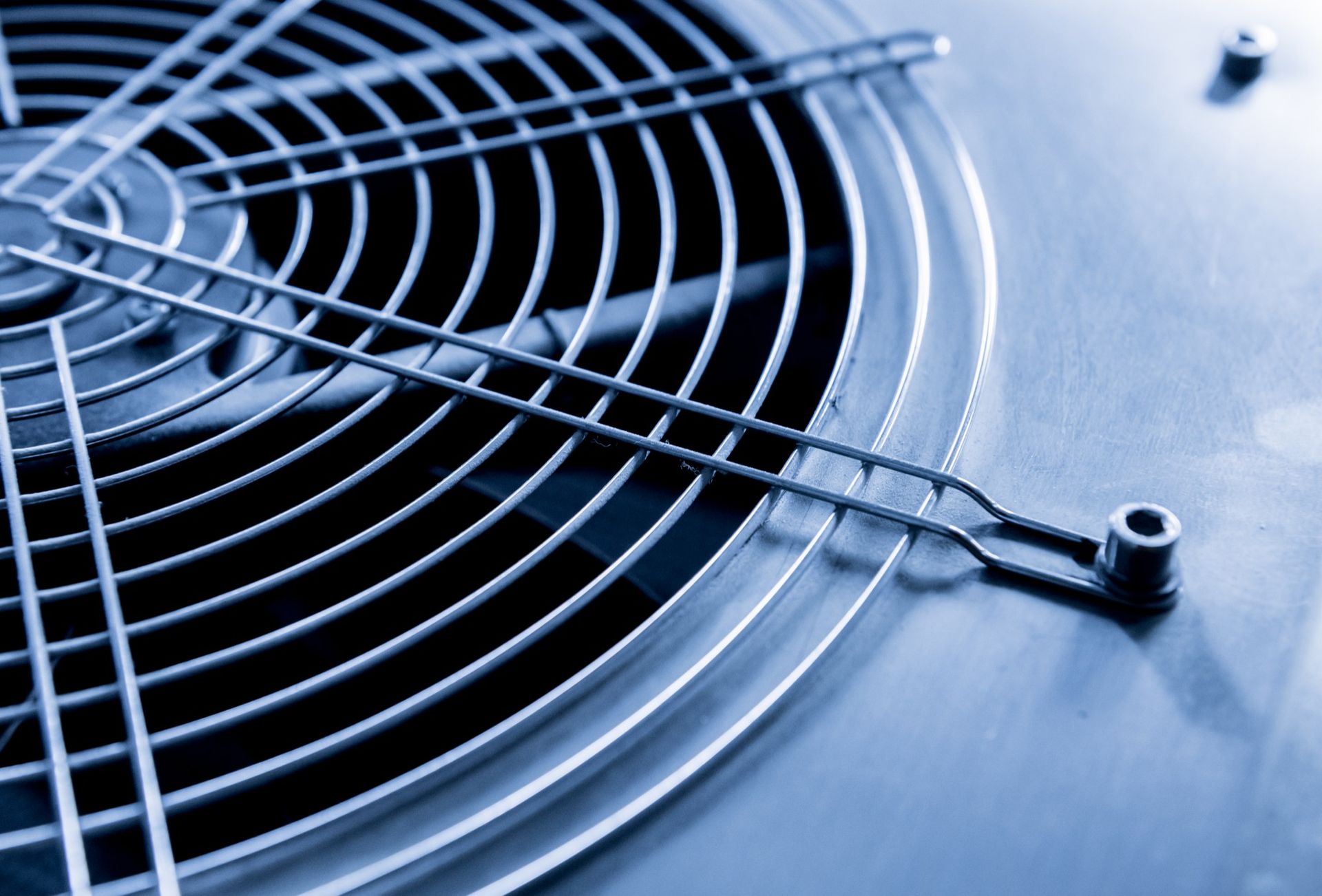 Close-up of a metal fan grille and blades, tinted blue.