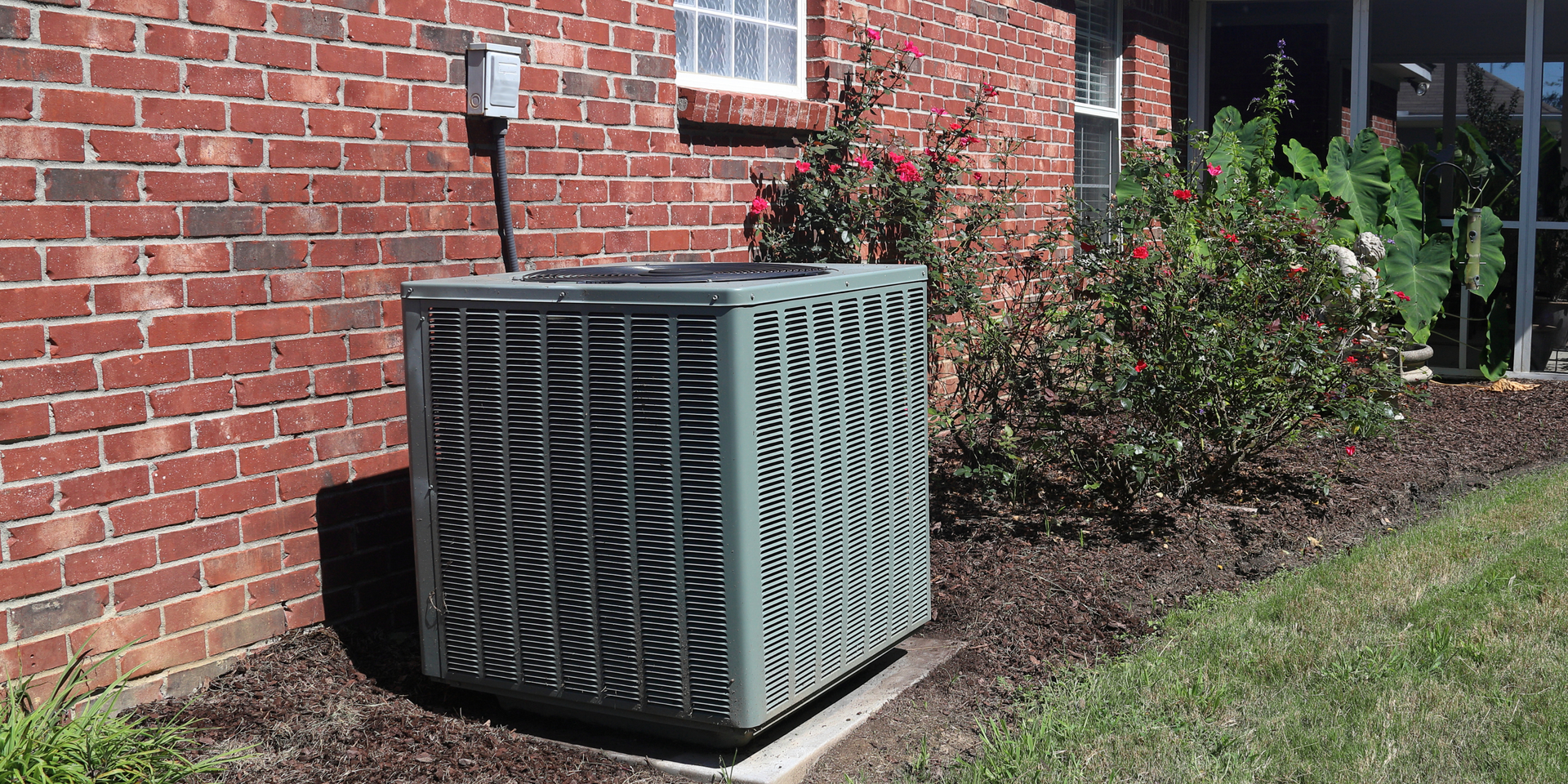 Outdoor HVAC unit beside a brick house, with a lattice cover on a sunny lawn