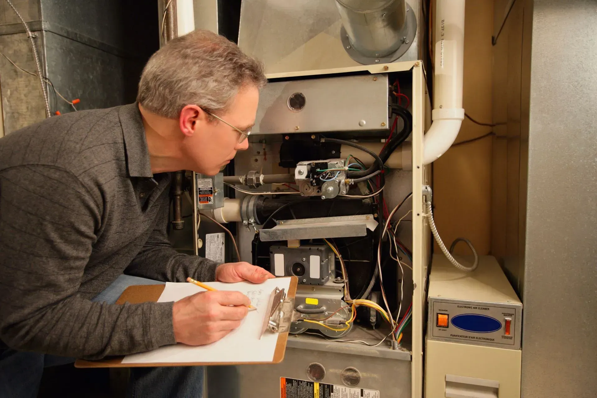 Technician inspecting the open furnace with a clipboard in a utility room