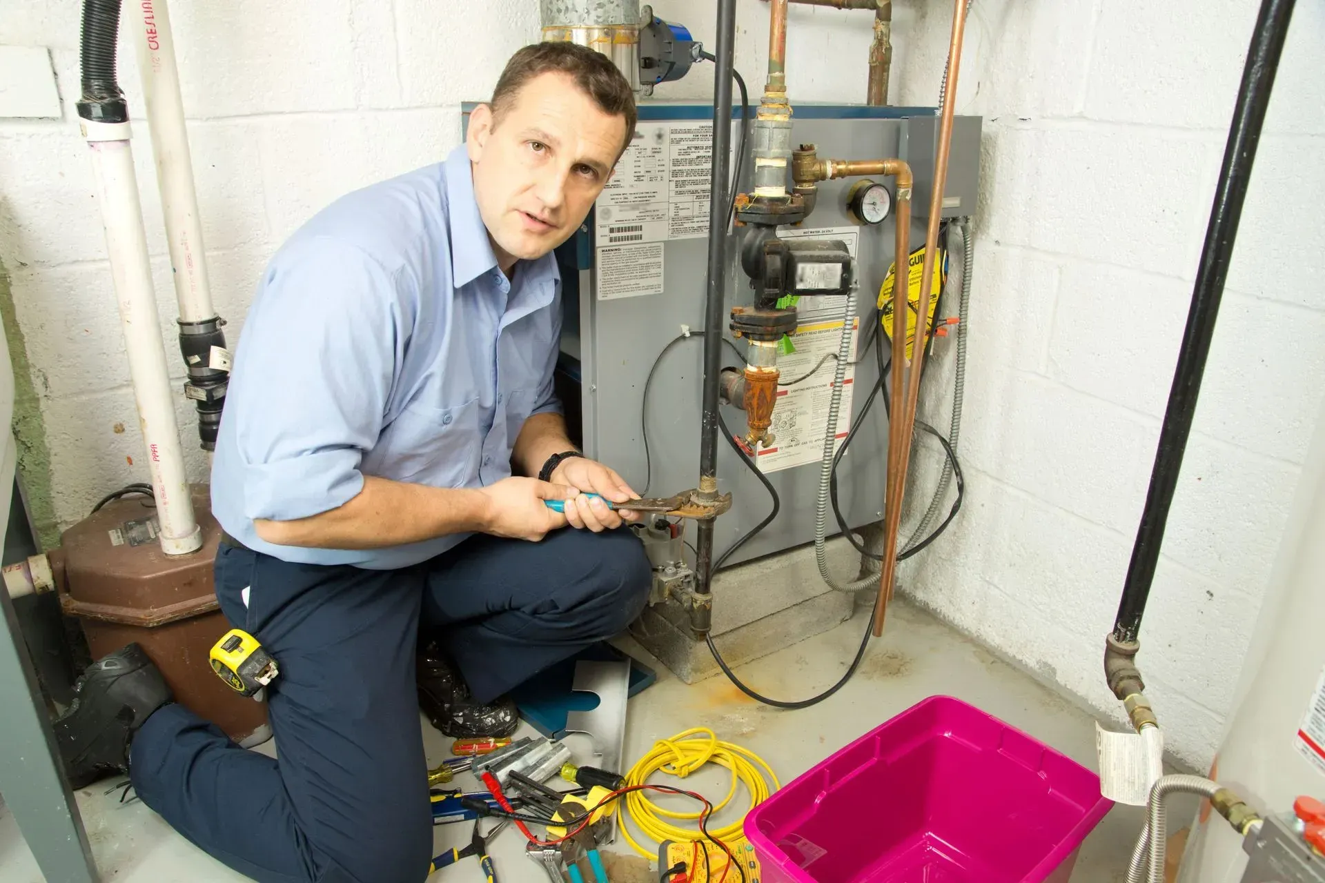 Technician kneels beside a furnace, inspecting wiring with tools in a utility room.